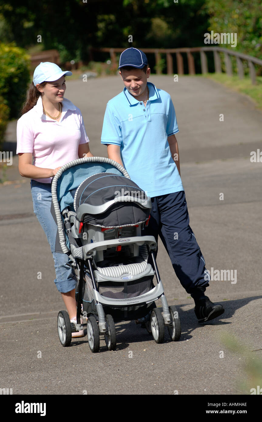 Un ragazzo adolescente e una ragazza vestita come chavs camminare il loro bambino in un contenuto della PRAM Foto Stock