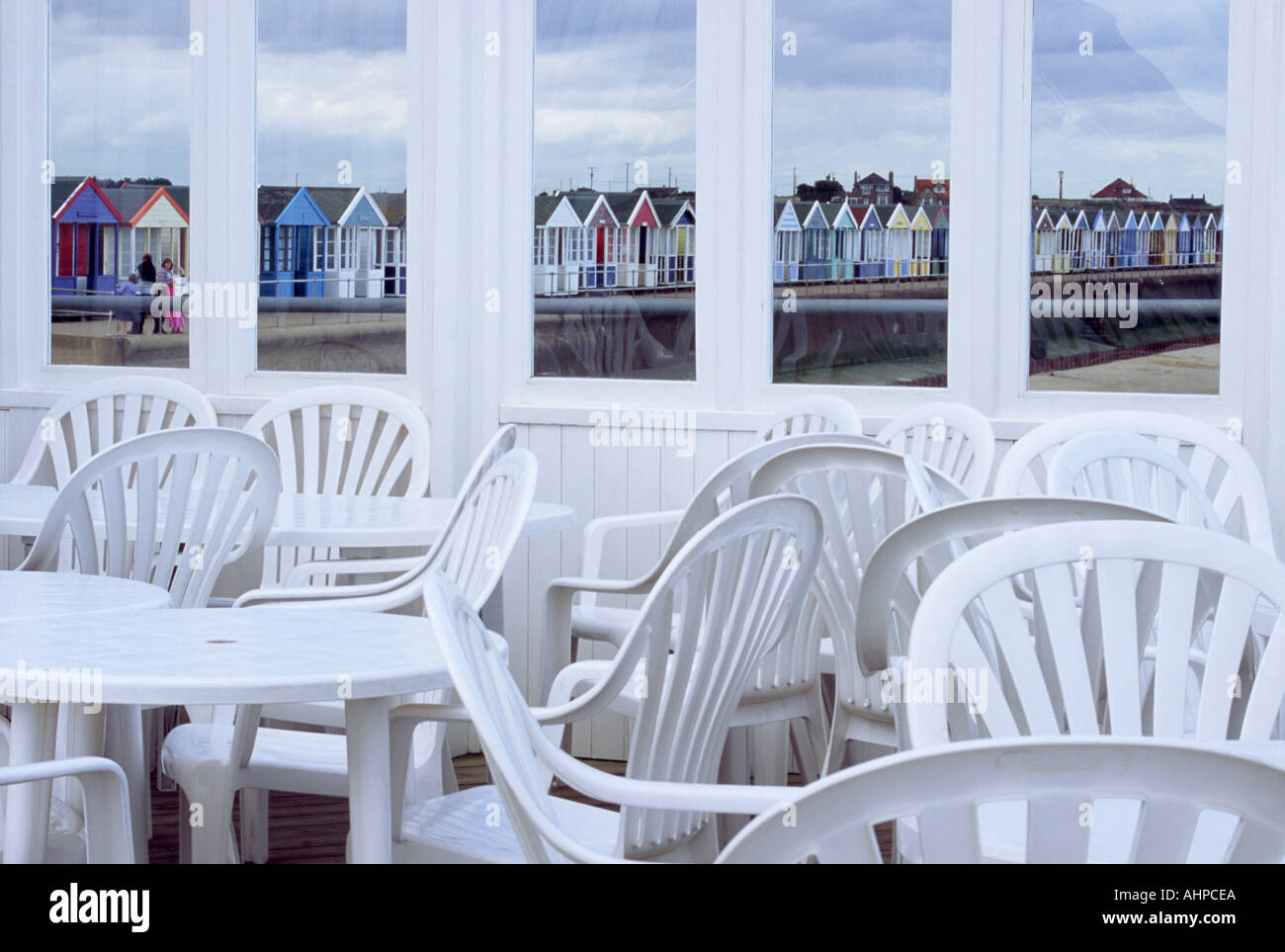 Tavoli e sedie su Southwold Pier con vedute della spiaggia di capanne tramite Windows Foto Stock