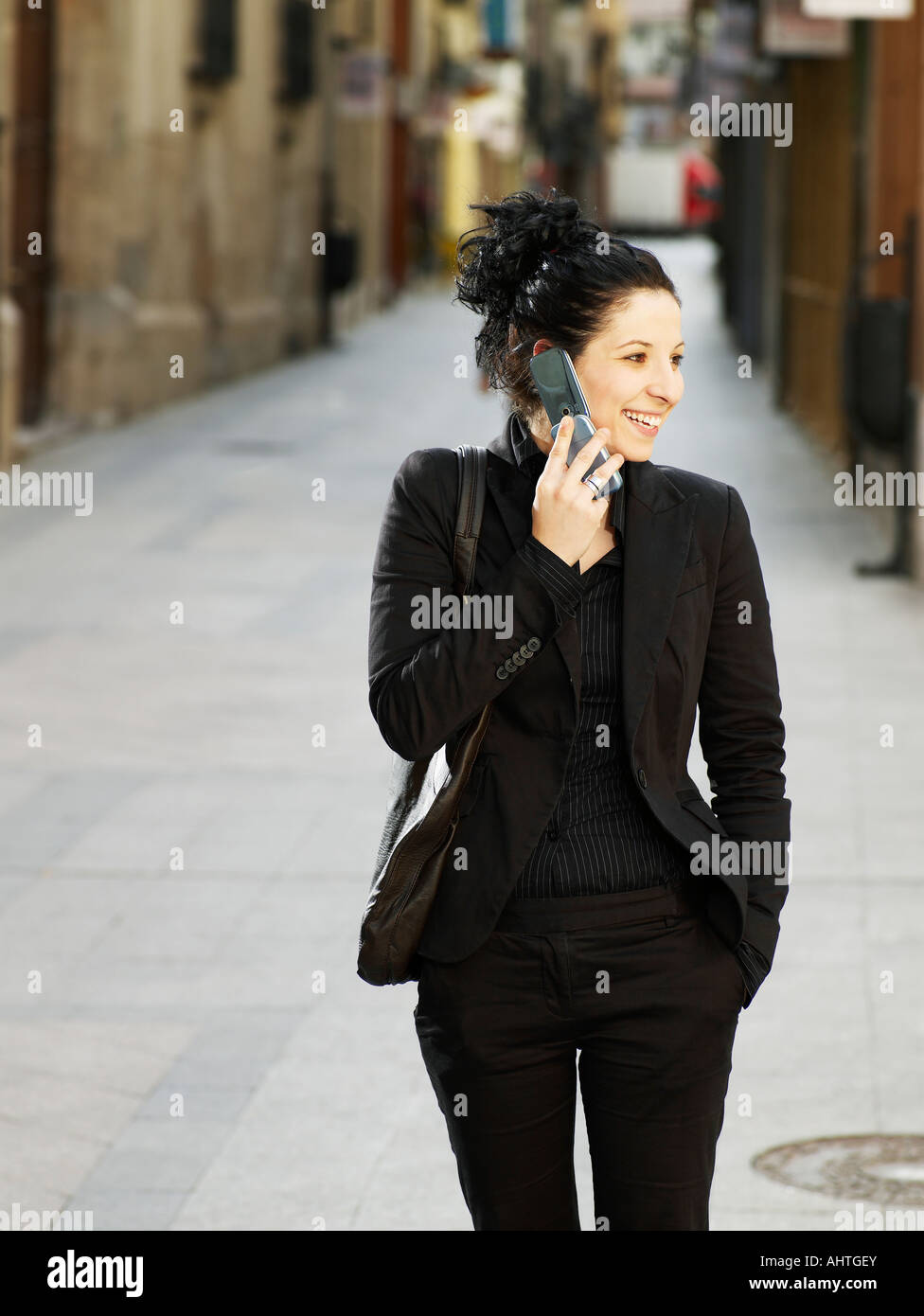 Giovane donna a piedi in strada utilizzando il telefono cellulare, sorridente Foto Stock