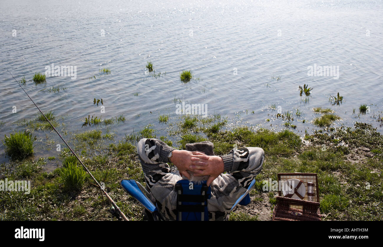 Senior uomo pesca da fiume, seduto con le mani dietro la testa, vista posteriore Foto Stock