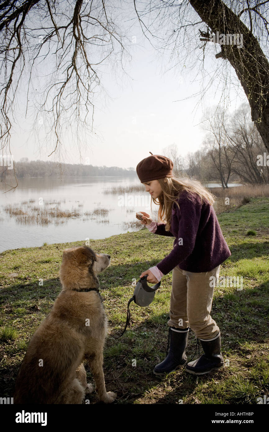 La ragazza (10-12) in piedi dal fiume holding pezzo di torta nella parte anteriore del cane Foto Stock