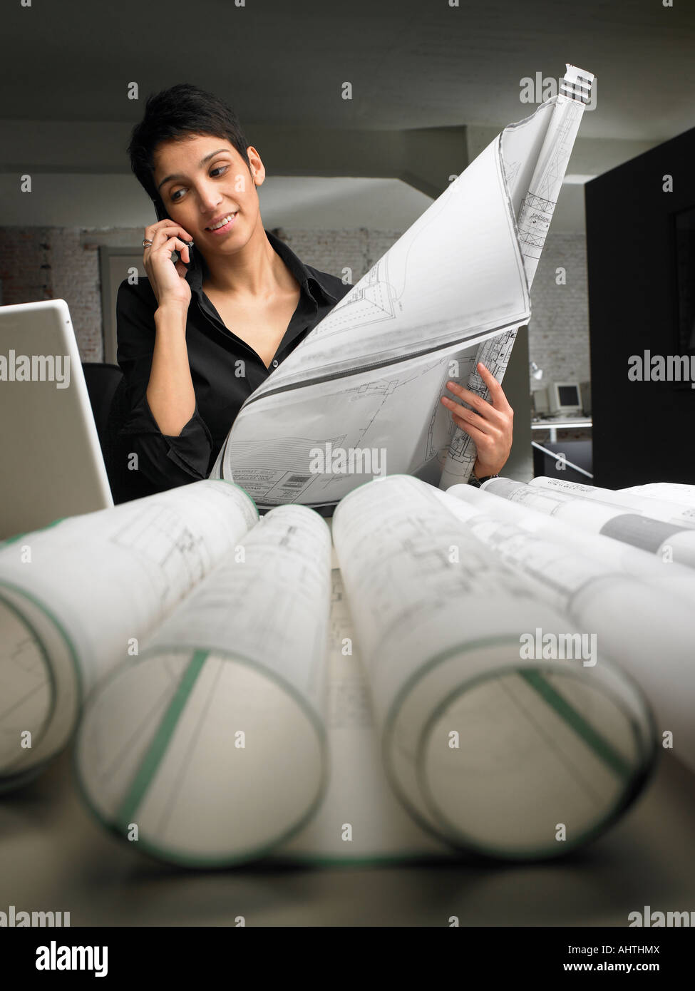 Architetto femmina parlando al telefono mentre blueprint di lettura alla scrivania. Bruxelles, Belgio. Foto Stock