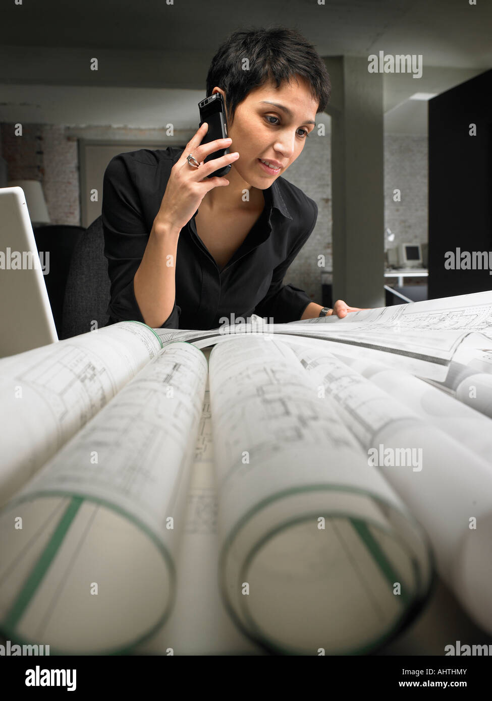 Architetto femmina tramite telefono cellulare, guardando i piani sulla scrivania Foto Stock