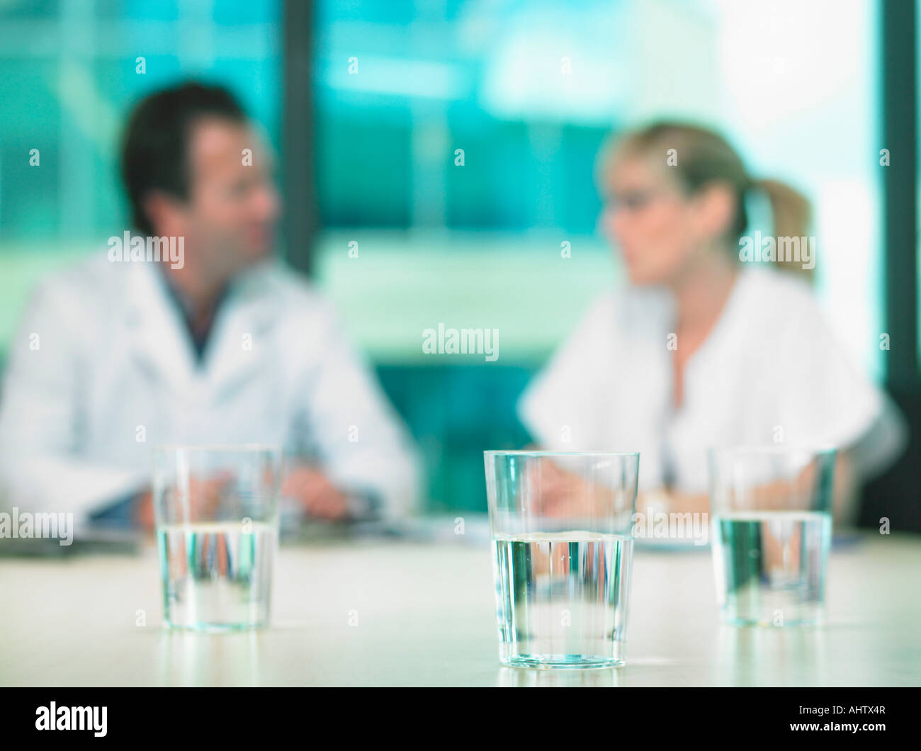 Due medici in una riunione di affari. Al di fuori della messa a fuoco. Close up sui bicchieri di acqua in primo piano. Foto Stock