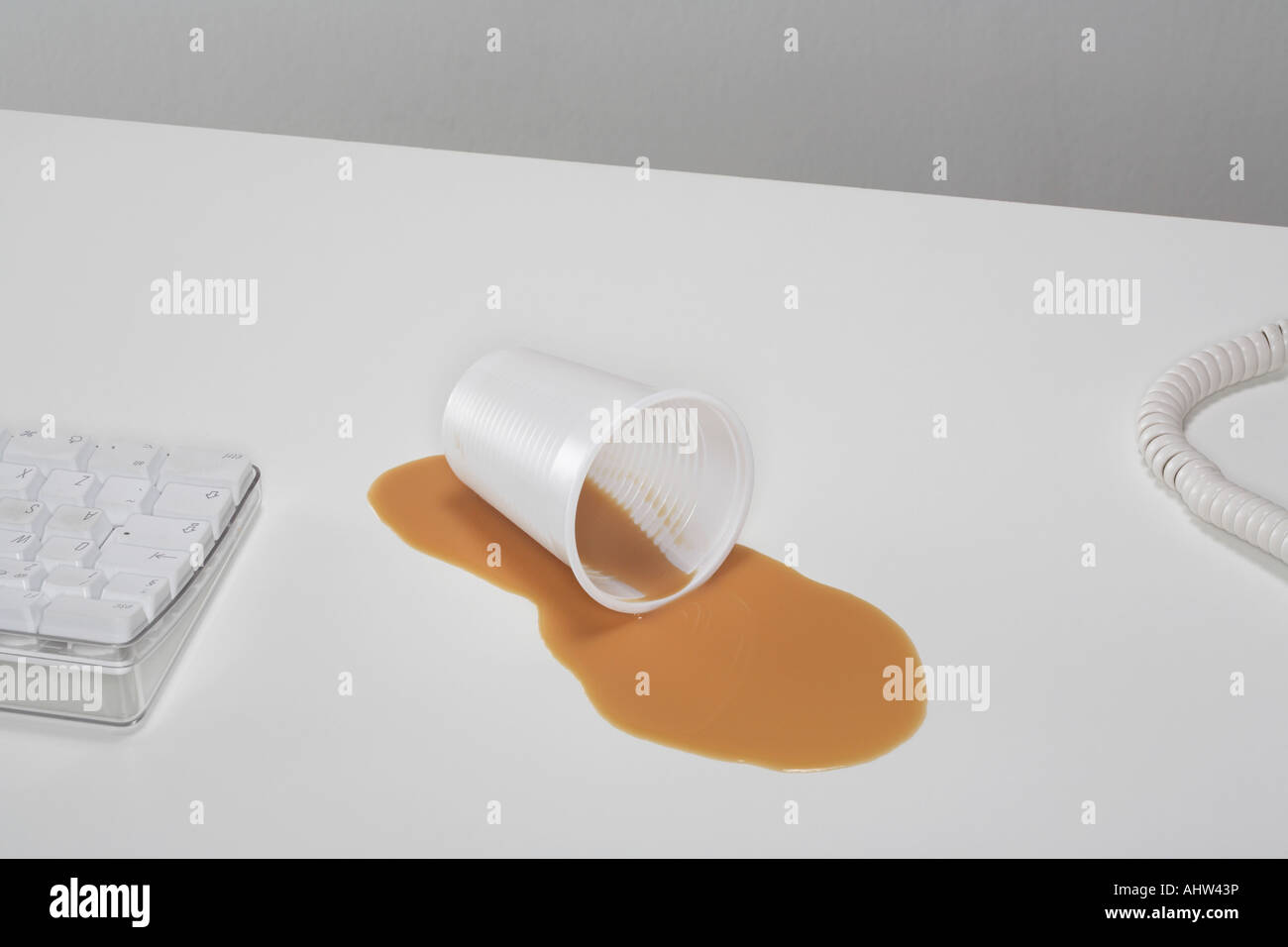 Un bicchiere di plastica consiste in un pool di tè versato su una scrivania. Foto Stock