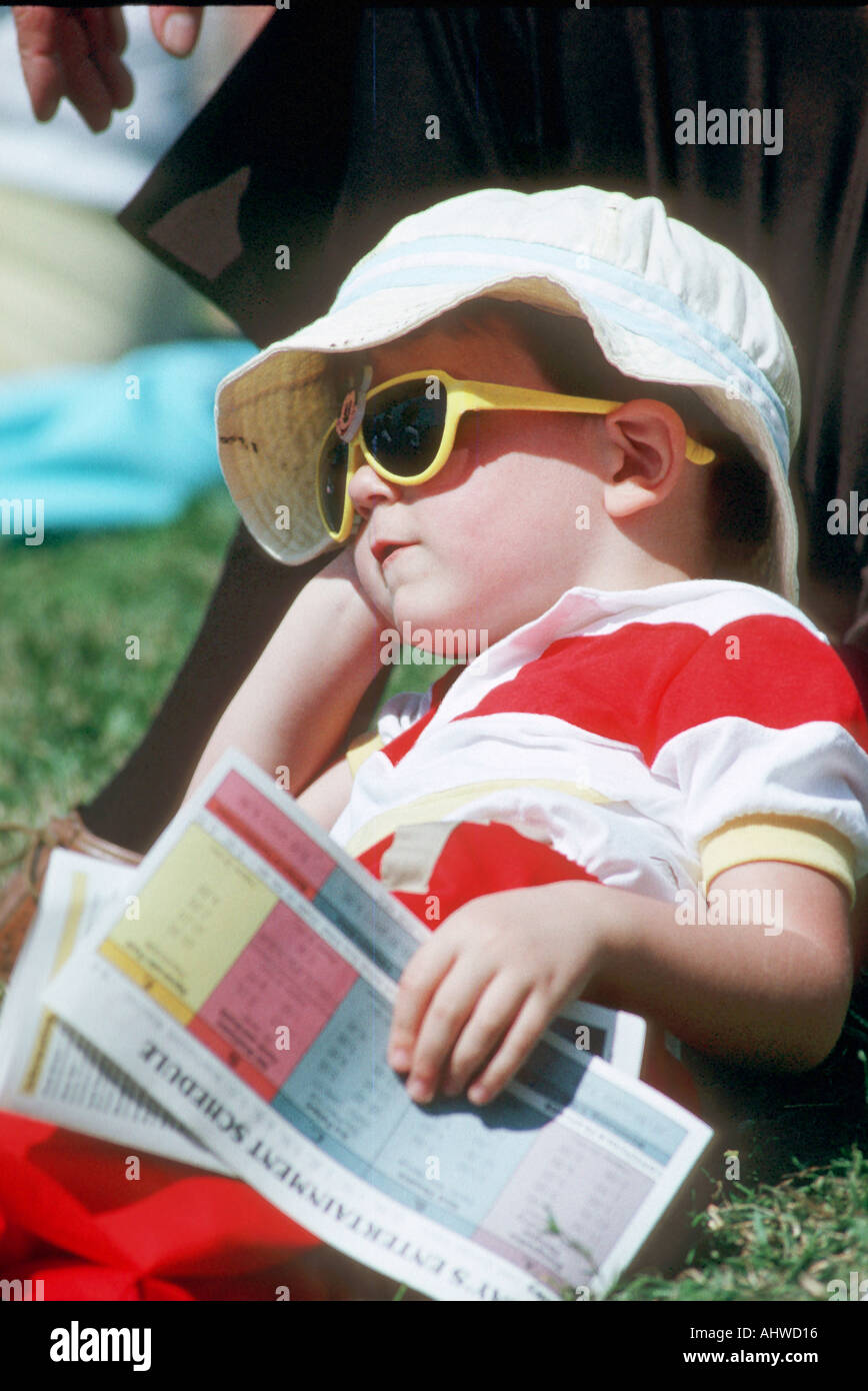 18 mese Ragazzo con occhiali da sole quotidiano e il cappuccio si appoggia contro i padri gamba grafica umoristica Foto Stock