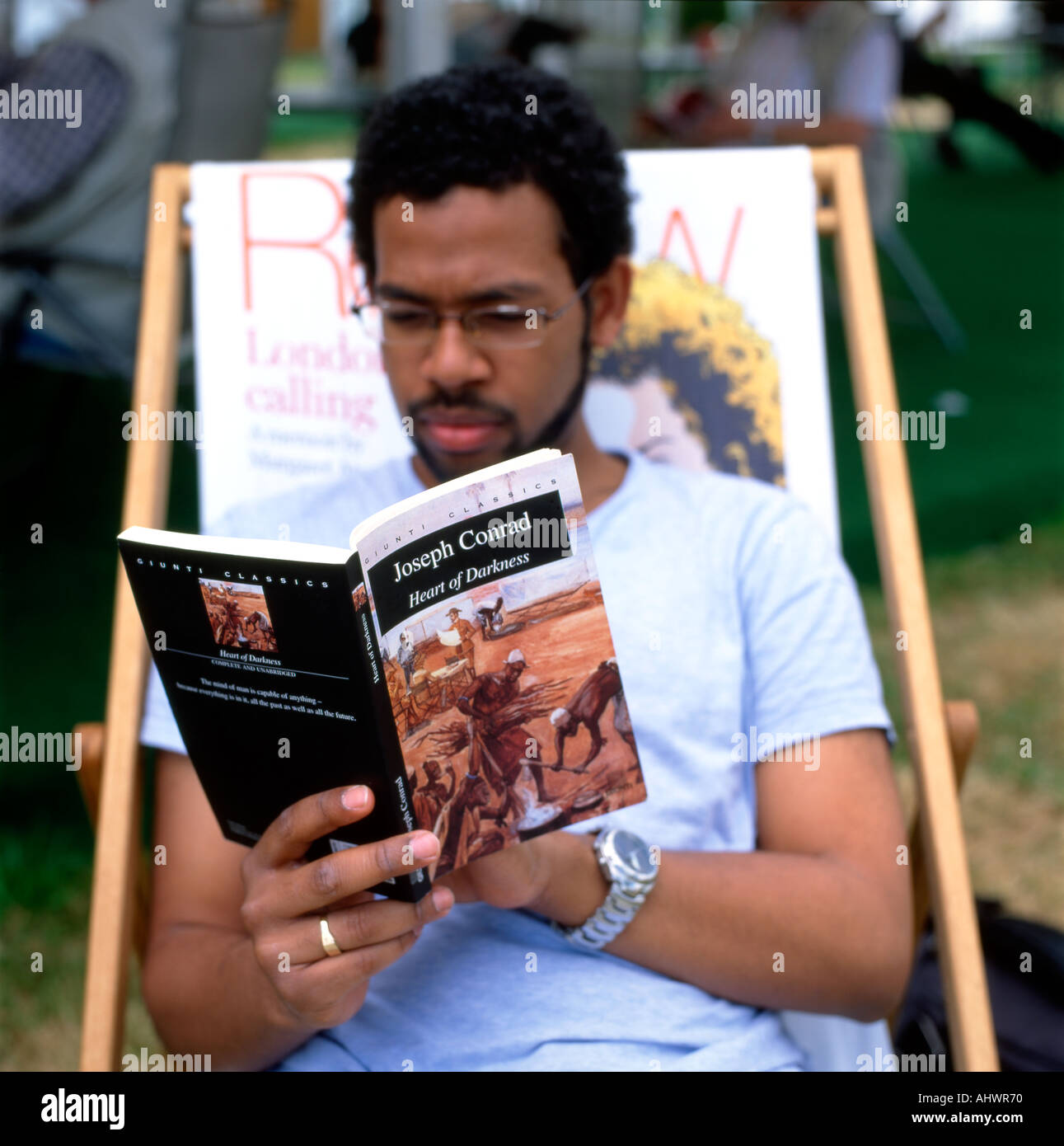 Giovane uomo nero seduto in una sedia a sdraio leggere Joseph Conrad romanzo africano del libro cuore di oscurità al Festival di Hay a Hay su Wye UK KATHY DEWITT Foto Stock