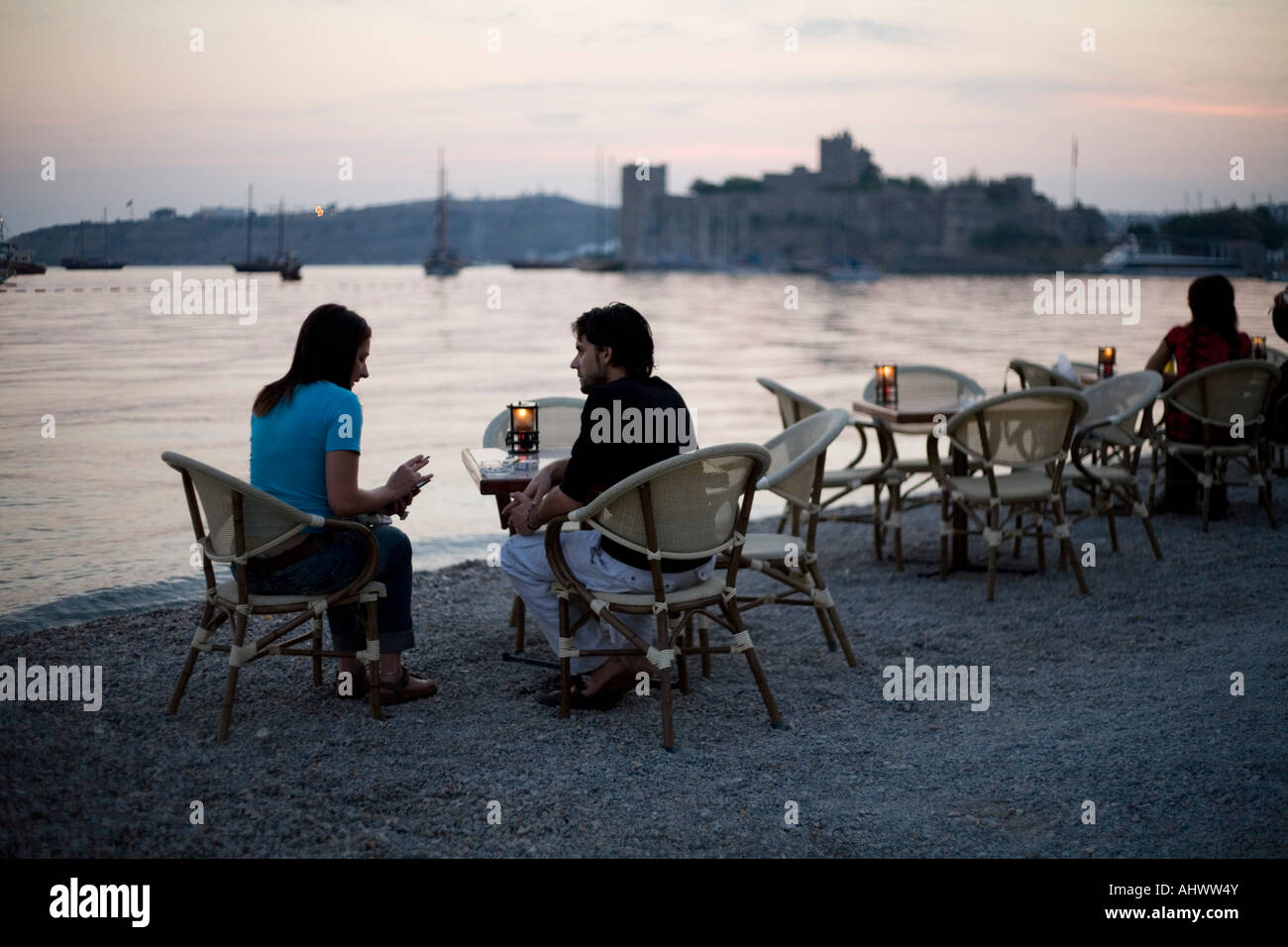 Coppia avente un drink sulla Spiaggia di Bodrum con castello in backround Foto Stock