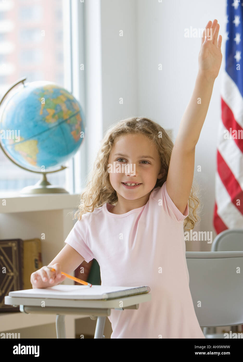 Ragazza alzando la mano al banco di scuola Foto Stock