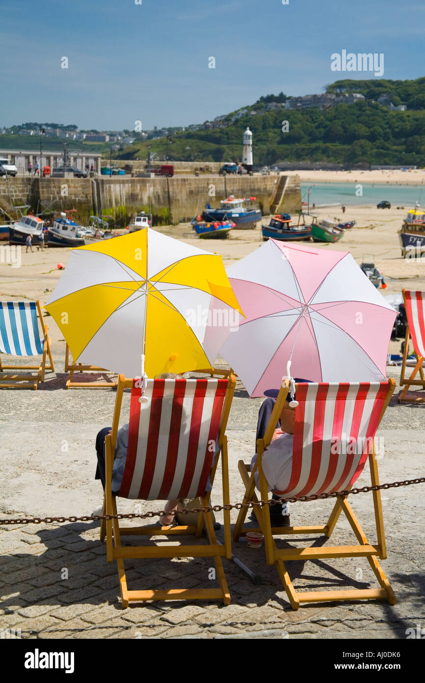 Due 2 sedie a sdraio Sedie a sdraio con gli occupanti riparo dal sole sotto ombrelloni ombrellone St Ives harbour UK GB Foto Stock