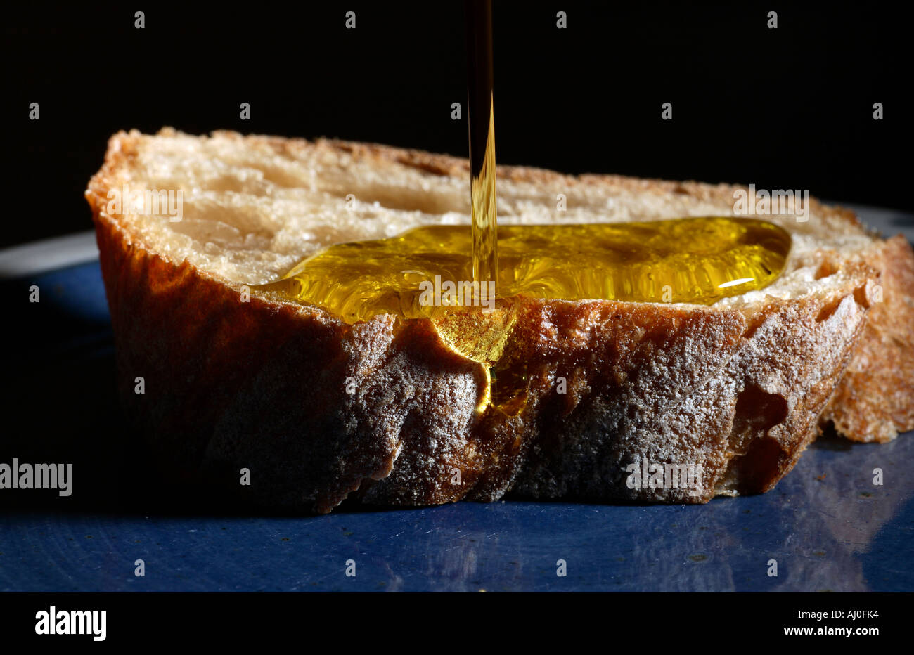 Olio di oliva versando sulla fetta di pane. Foto Stock