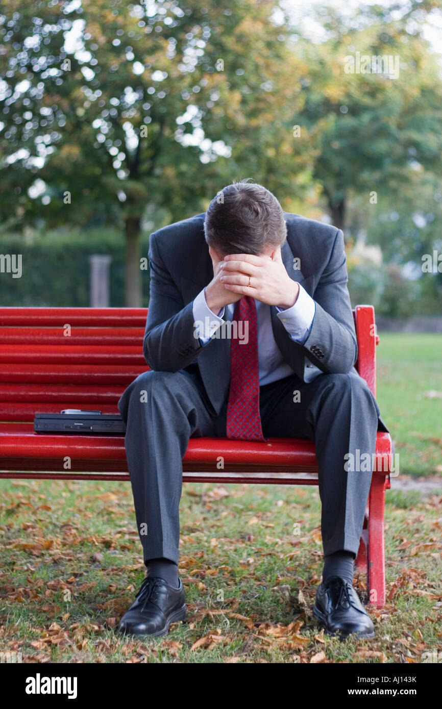 Preoccupato imprenditore seduto su una rossa una panchina nel parco Foto Stock