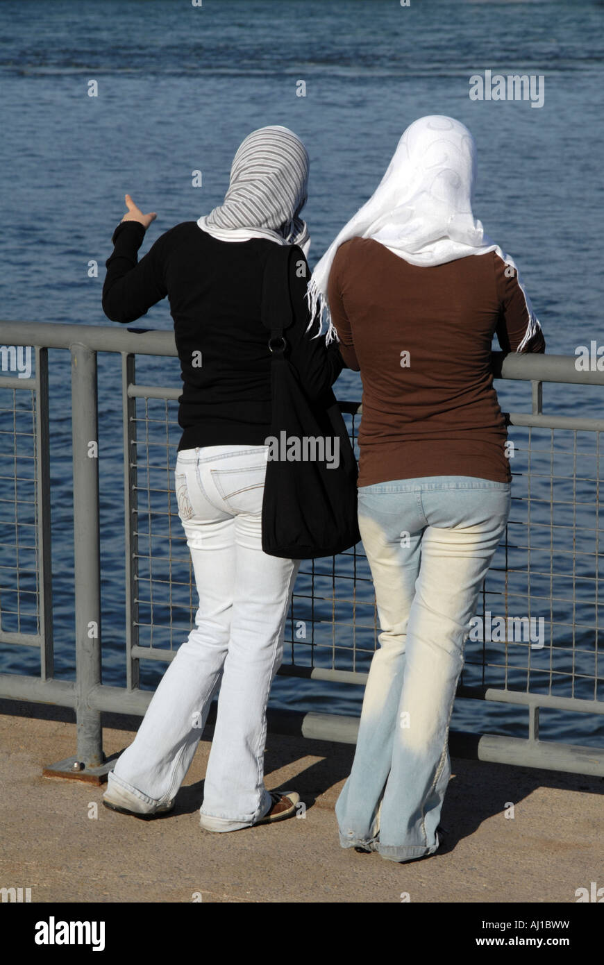 Due giovani ragazze che indossano hijab sono rivolti e guardando all'estero su un corpo di acqua Foto Stock