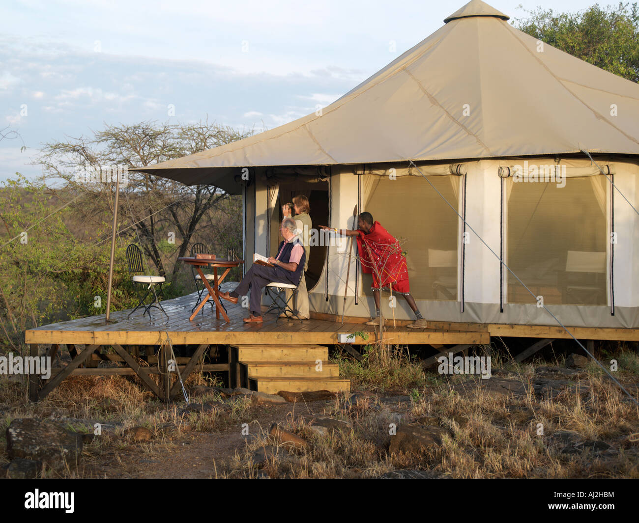 Una guida Masai ricorda un animale selvatico ai visitatori sulla veranda della tenda theircomfortable a Ol Seki Tented Camp Foto Stock