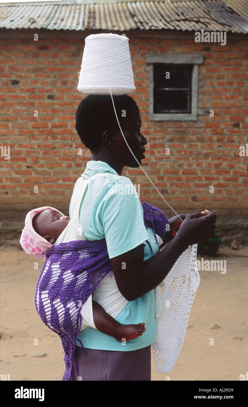La donna a crochet da un rocchetto di filo di cotone equilibrato sul suo capo mentre portando il suo bambino sulla schiena e a piedi lungo i. Zimbabwe Foto Stock