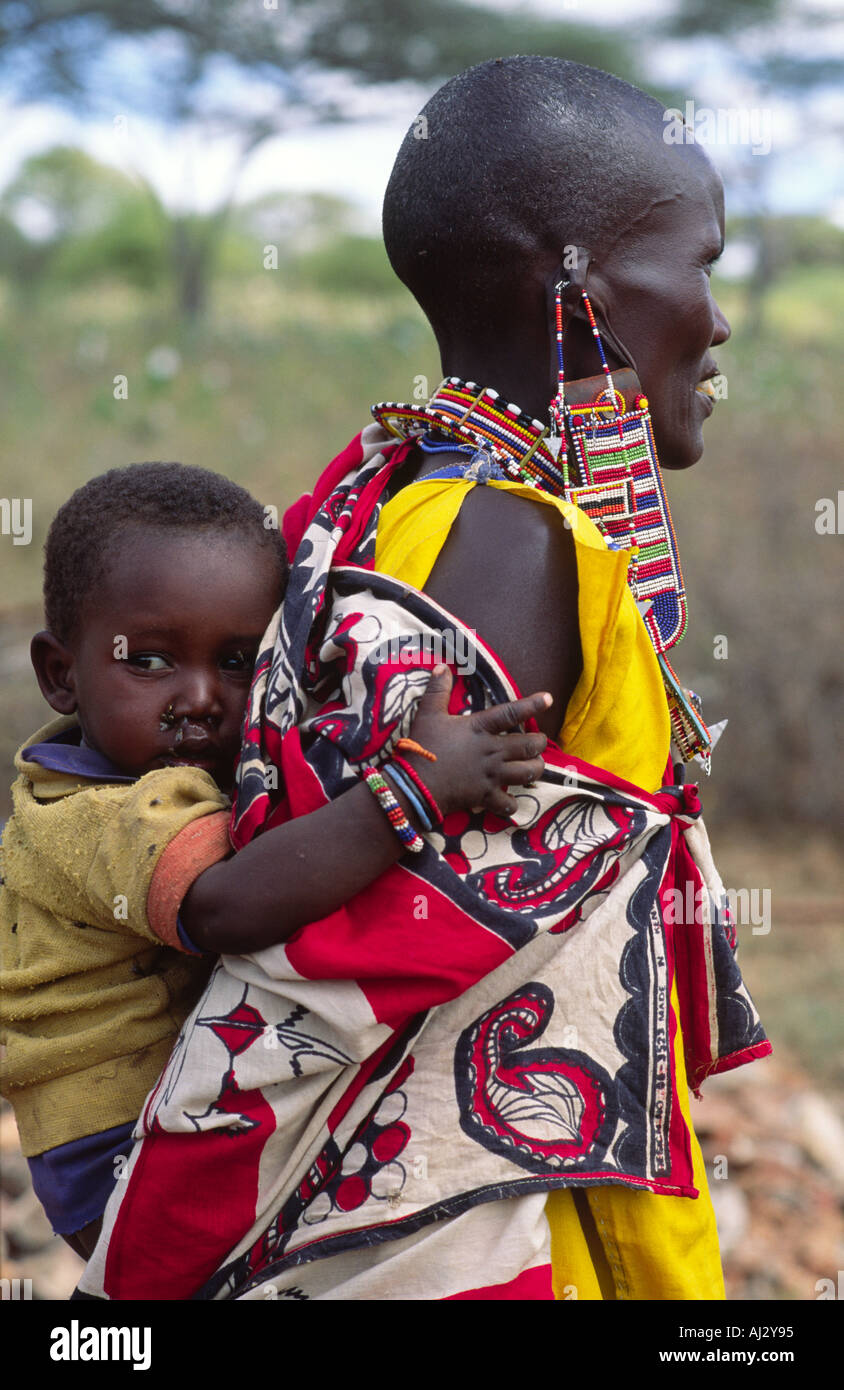 Vista laterale di una donna Maasai in tradizionali abiti colorati e gioielli, portando il suo bambino sulla schiena. Kenya Foto Stock