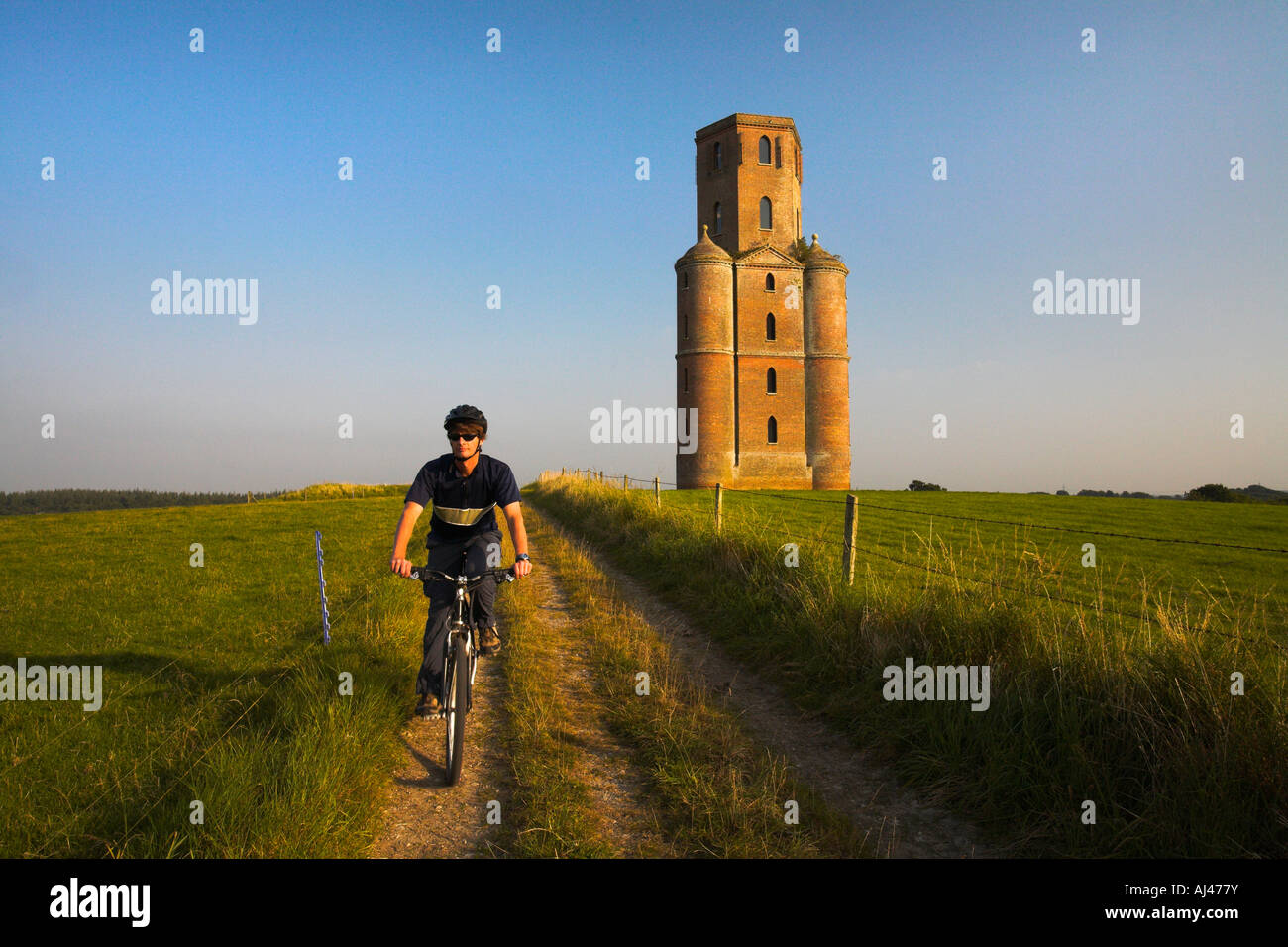 Ciclista su un fuori strada Trail passa accanto alla torre di Horton follia, Dorset Foto Stock