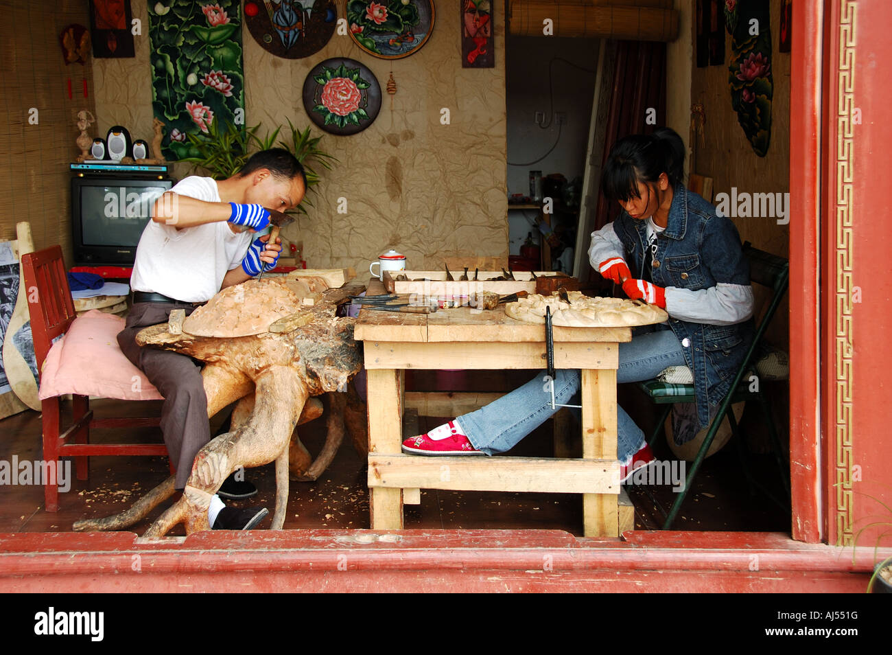 Un uomo e una donna che lavorano sulla loro legno scolpisce in una strada shop. Lijiang, Yunnan, Cina Foto Stock
