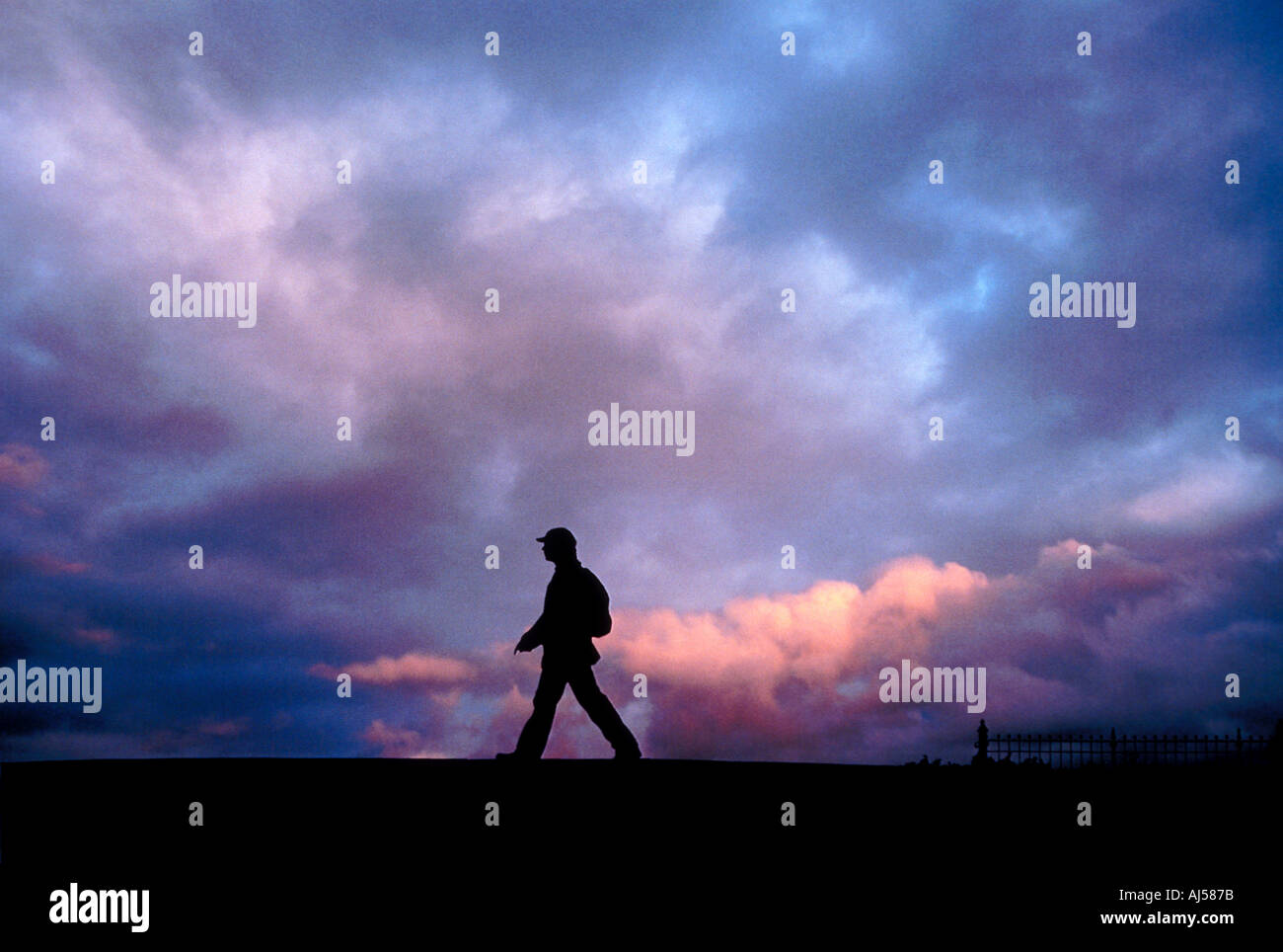 Silhouette di persona che cammina al tramonto come nuvole temporalesche sviluppare Foto Stock