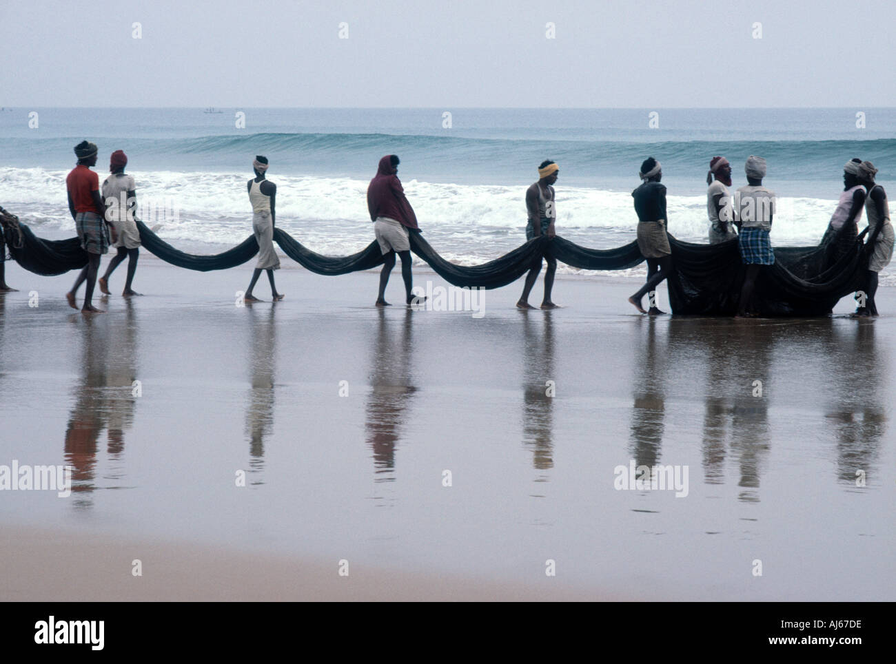 Caricamento dei pescatori le reti sulla loro barca sulla spiaggia all'alba Foto Stock