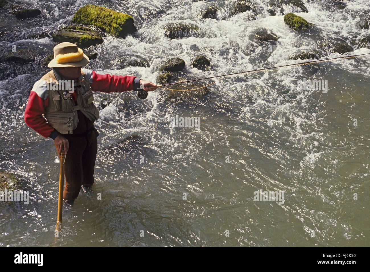 Pescatore a mosca in piedi di scorrimento veloce flusso di trote utilizzando personale per sostenere il signor Foto Stock