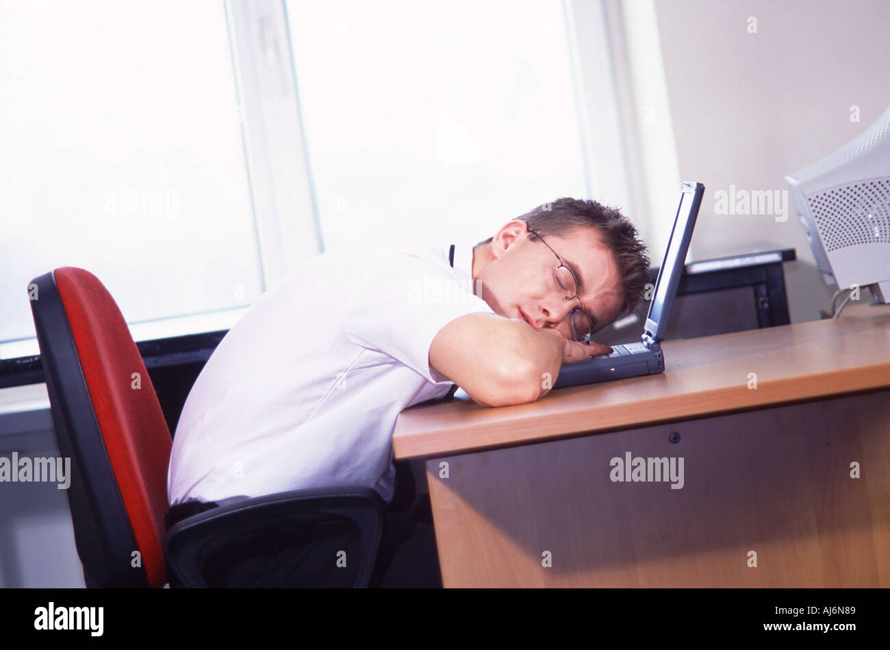 Giovane uomo in ufficio che dorme sul laptop. Foto Stock