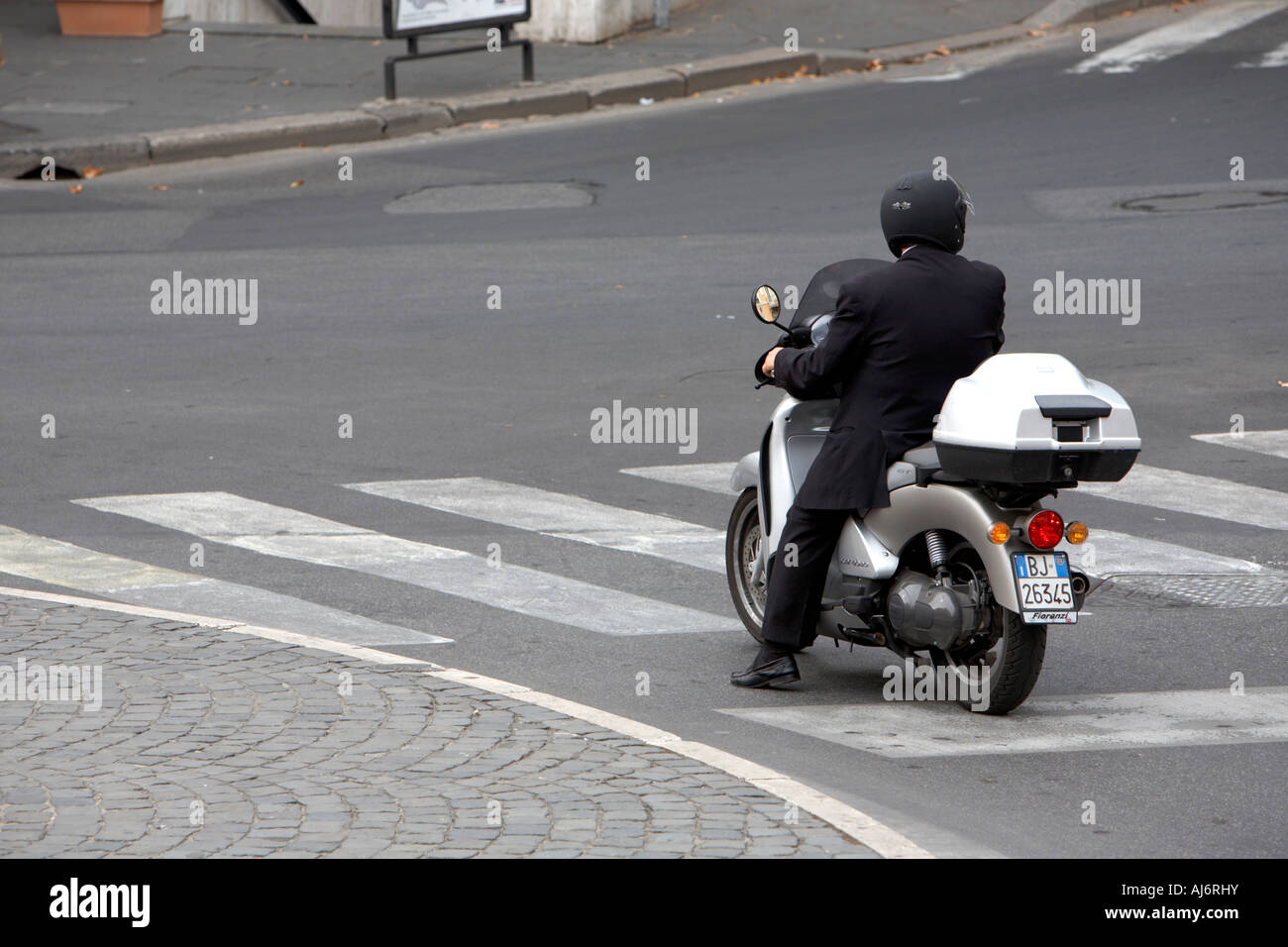 Imprenditore indossare tuta e casco nero su scooter siede all'attraversamento pedonale Roma Lazio Italia Foto Stock