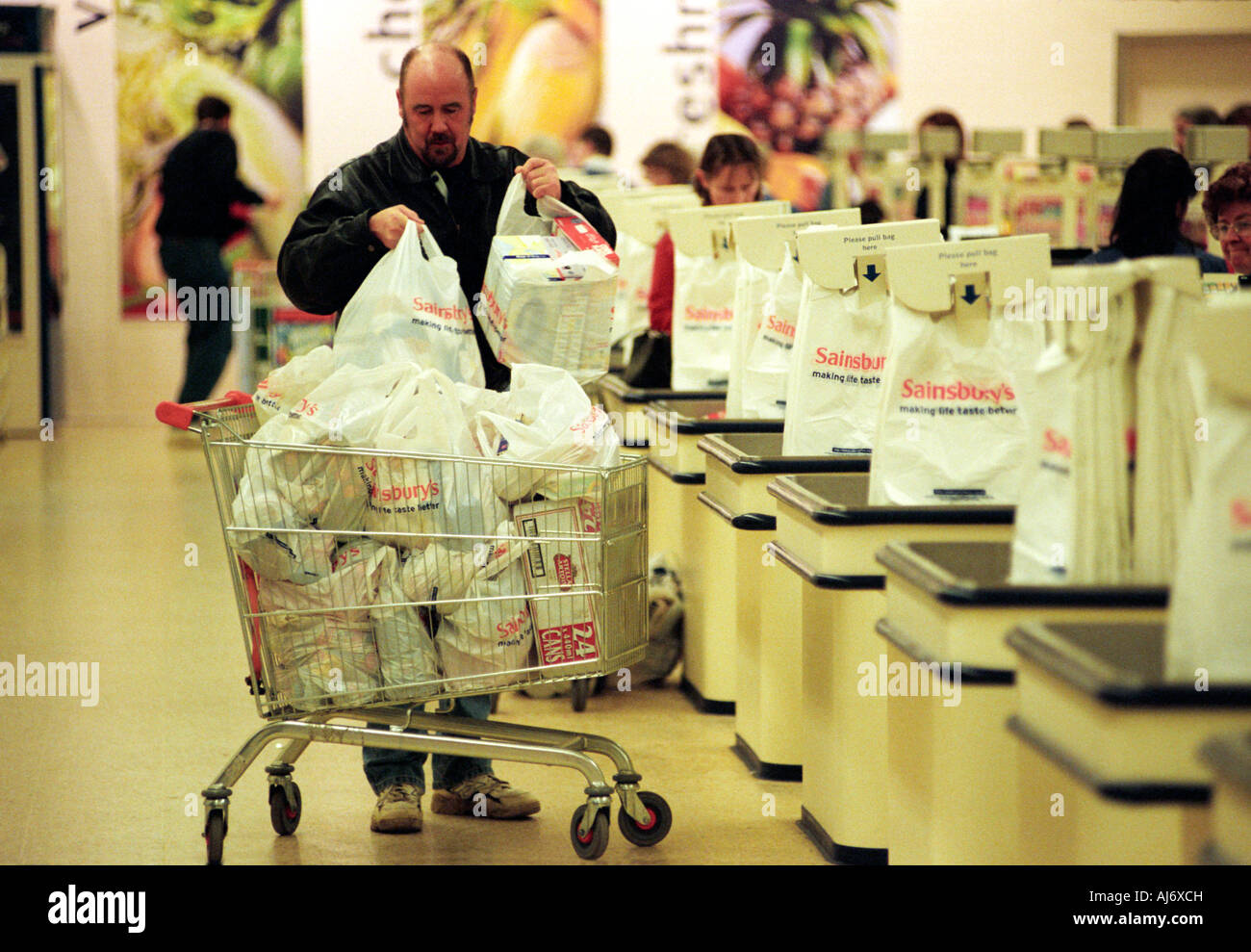 Un uomo di caricamento di un carrello della spesa con le borse della spesa in Sainsbury's supermercato Foto Stock