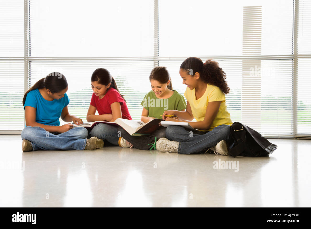 Preteen ragazze di etnie multipli seduti insieme sul pavimento con compiti scolastici Foto Stock