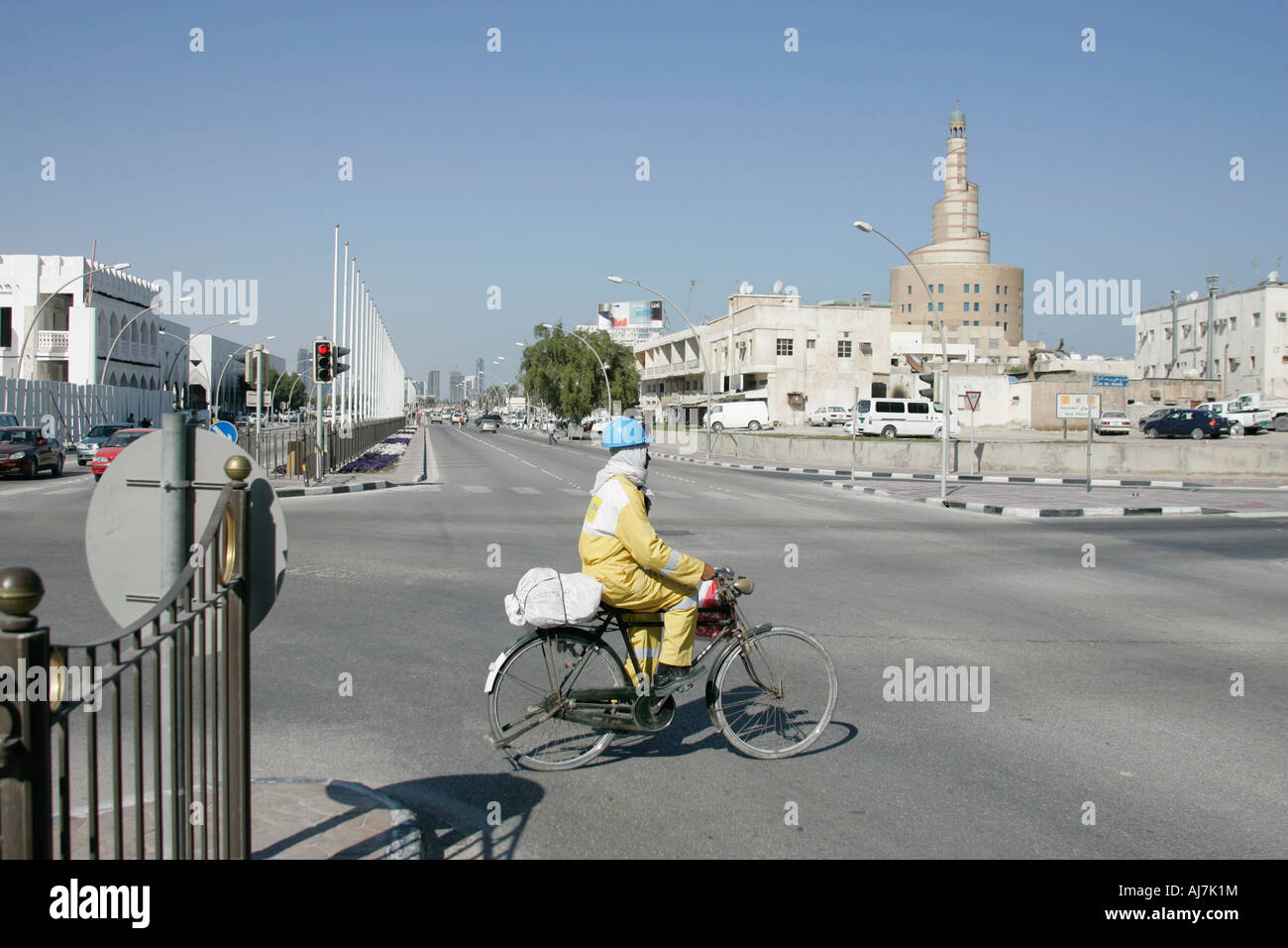 Operaio edile su una bicicletta attraversando la strada principale a Doha, in Qatar. Foto Stock