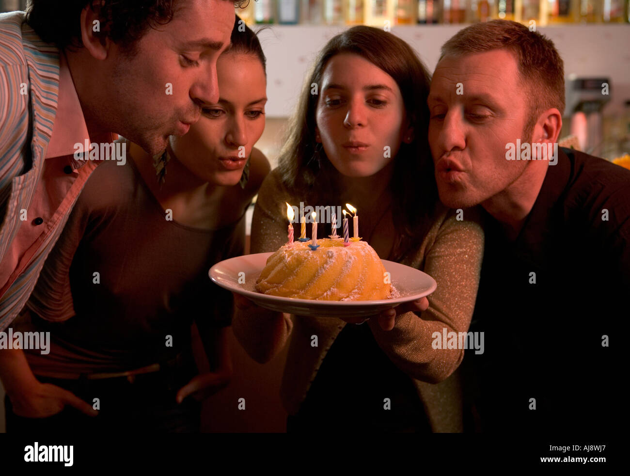 Gruppo di amici soffiando fuori candele sulla torta di compleanno Foto Stock