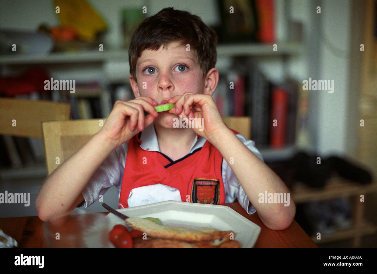 Un giovane ragazzo di mangiare la pizza e insalate a casa indossando un vecchio arsenale soccer shirt, Londra, Regno Unito. Foto Stock