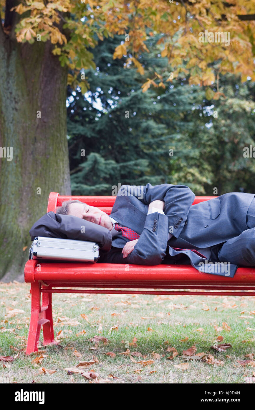 Imprenditore di dormire su un rosso parkbench in autunno Foto Stock
