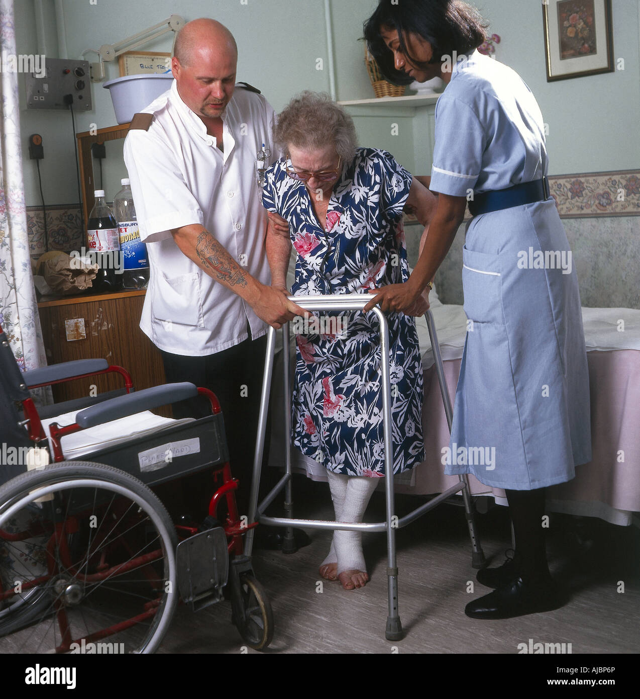 Un paziente anziano usando un Zimmer frame con l'assistenza di personale medico Foto Stock