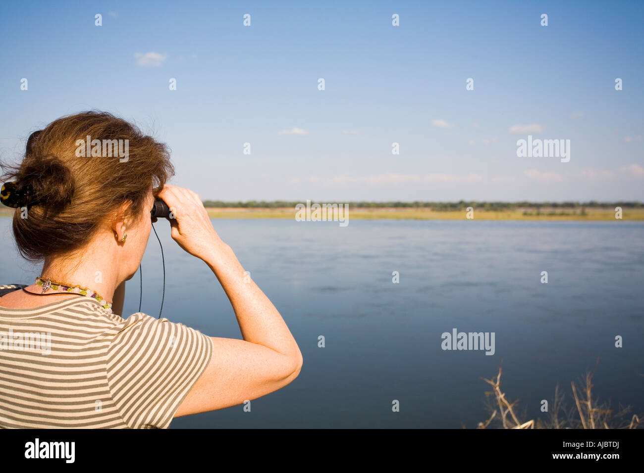 Donna matura guardando oltre il fiume Zambesi attraverso il binocolo Foto Stock