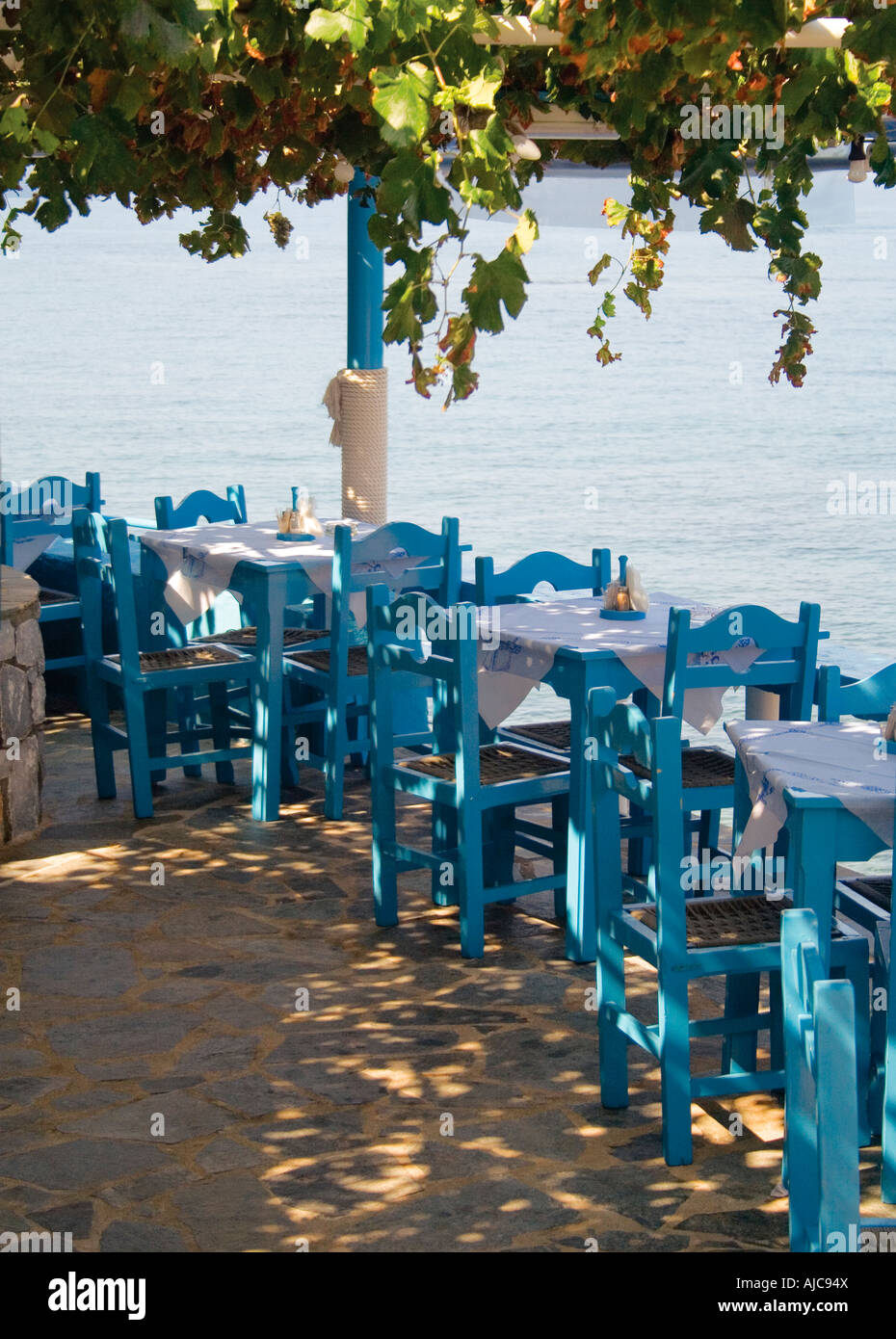 Ristorante affacciato sul mare in un porto di pesca, chiamato Stoupa, Grecia in estate con blue marine e i tavoli e le sedie e i vitigni Foto Stock