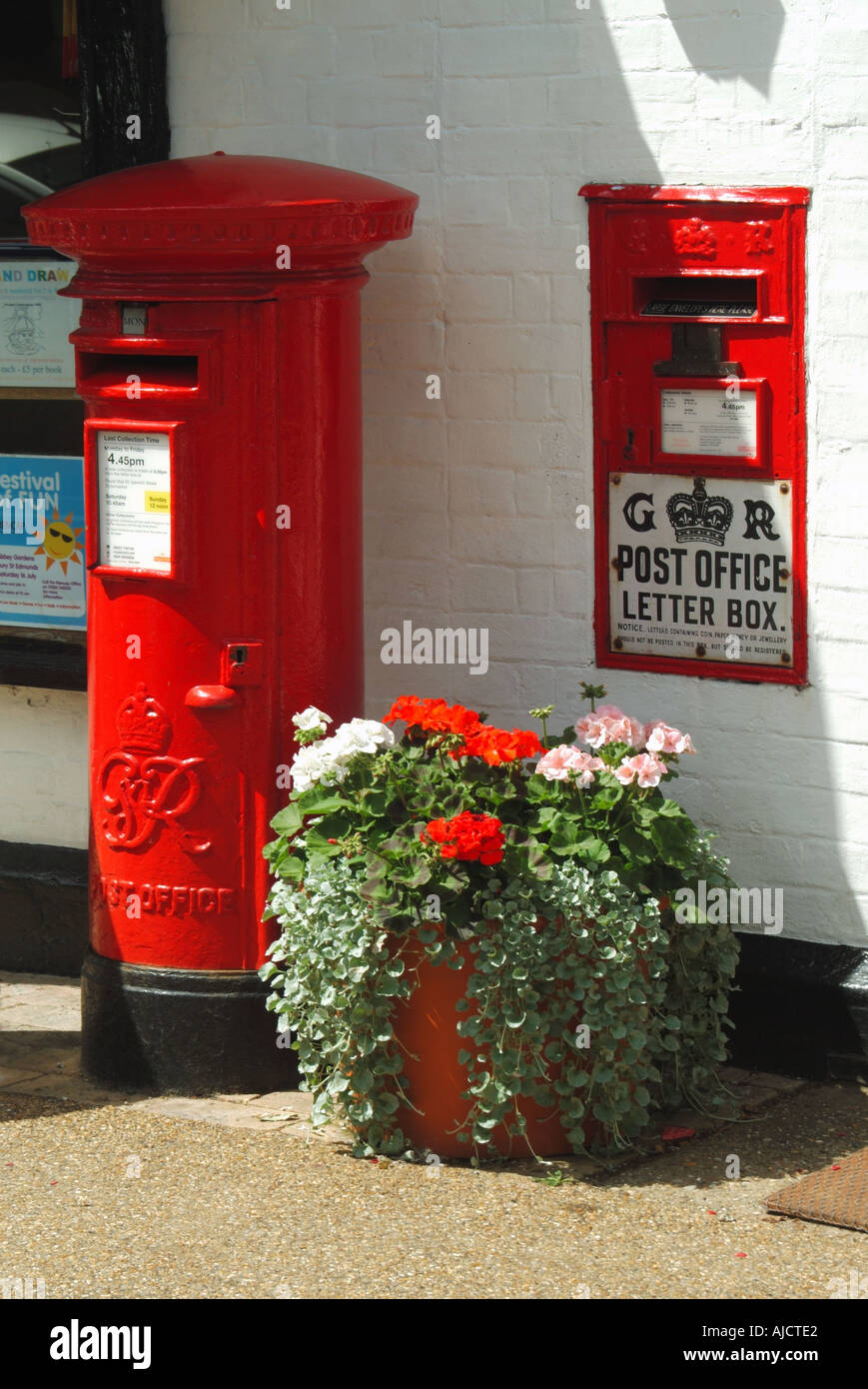 Woolpit villaggio due rosso GR caselle postali fuori villaggio di impianti di ufficio postale in fiore in vaso di fiori su pavimentazione giorno di sole nel Suffolk Inghilterra UK Foto Stock