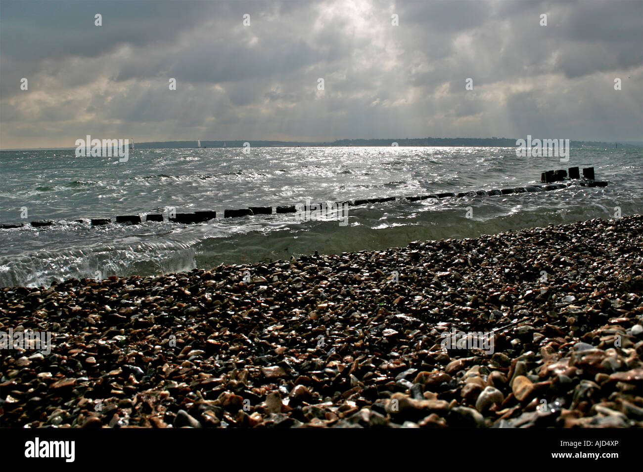 Acqua di Southampton, groyne in legno e la spiaggia di ciottoli insieme contro un imponente cielo a Calshot Spit, Calshot, Hampshire Foto Stock