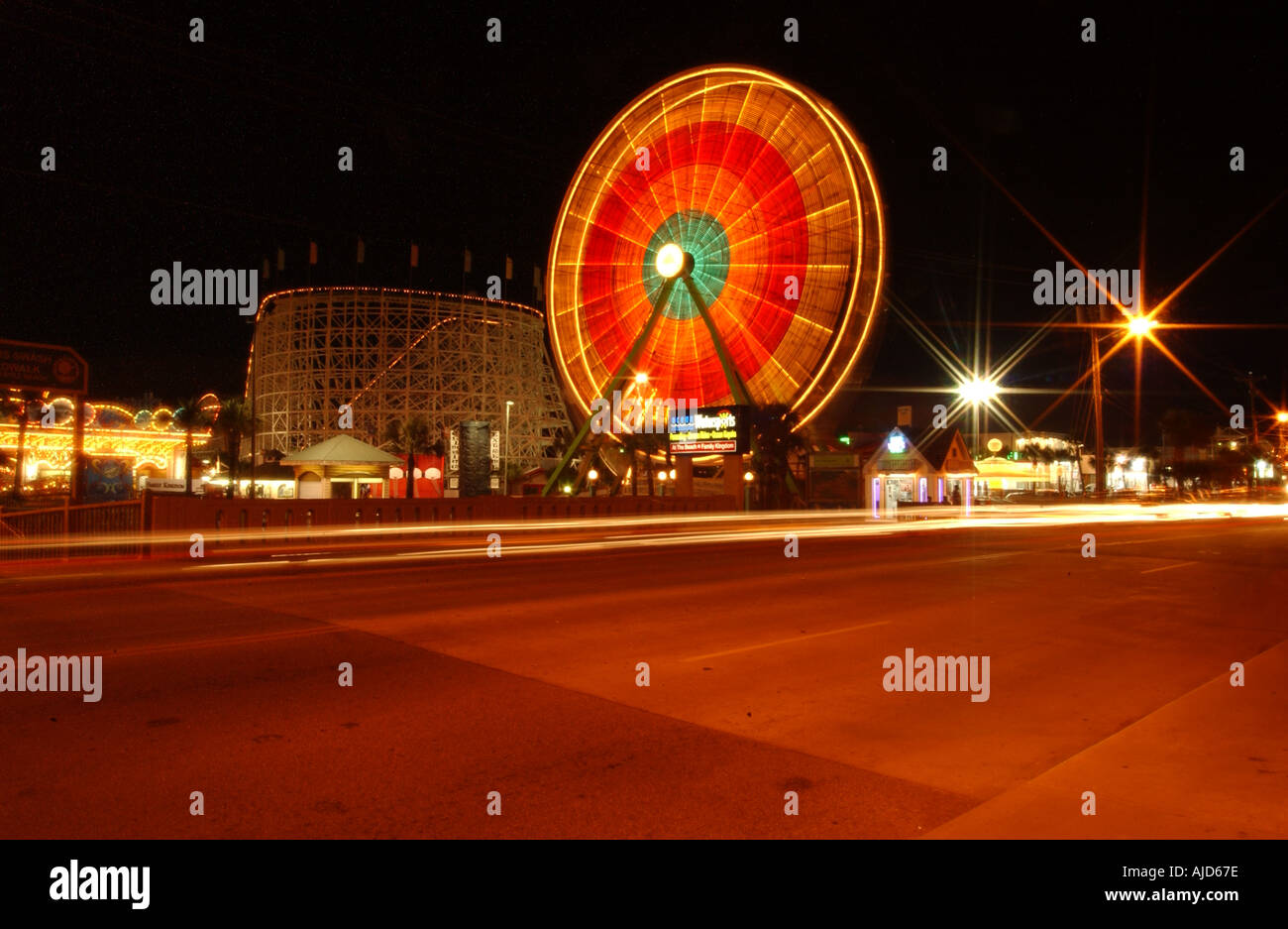 Orizzontale dell'immagine a colori immagine di una luminosa ruota panoramica Ferris offuscata dalla filatura di notte con le automobili che passa in primo piano Foto Stock