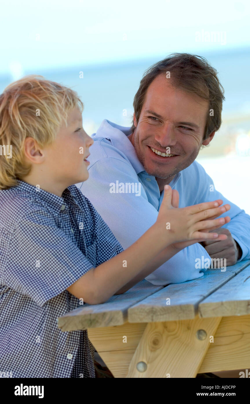 Padre e figlio seduti in spiaggia e parlare Foto Stock