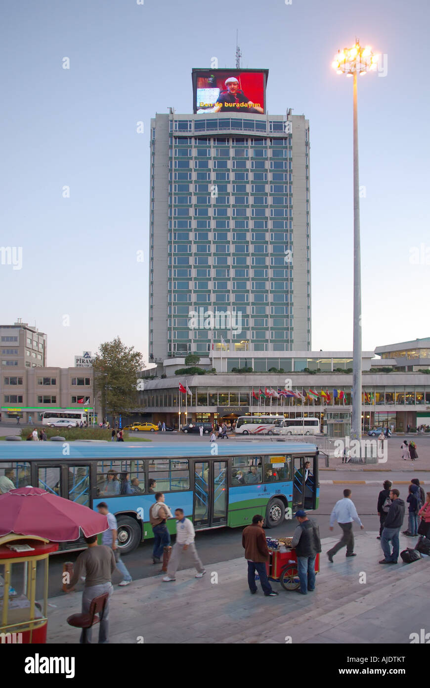 Istanbul Taksim Square autobus presso la stazione degli autobus di sera presto con la pubblicità elettronica pannello sul tetto di Marmara Hotel Foto Stock
