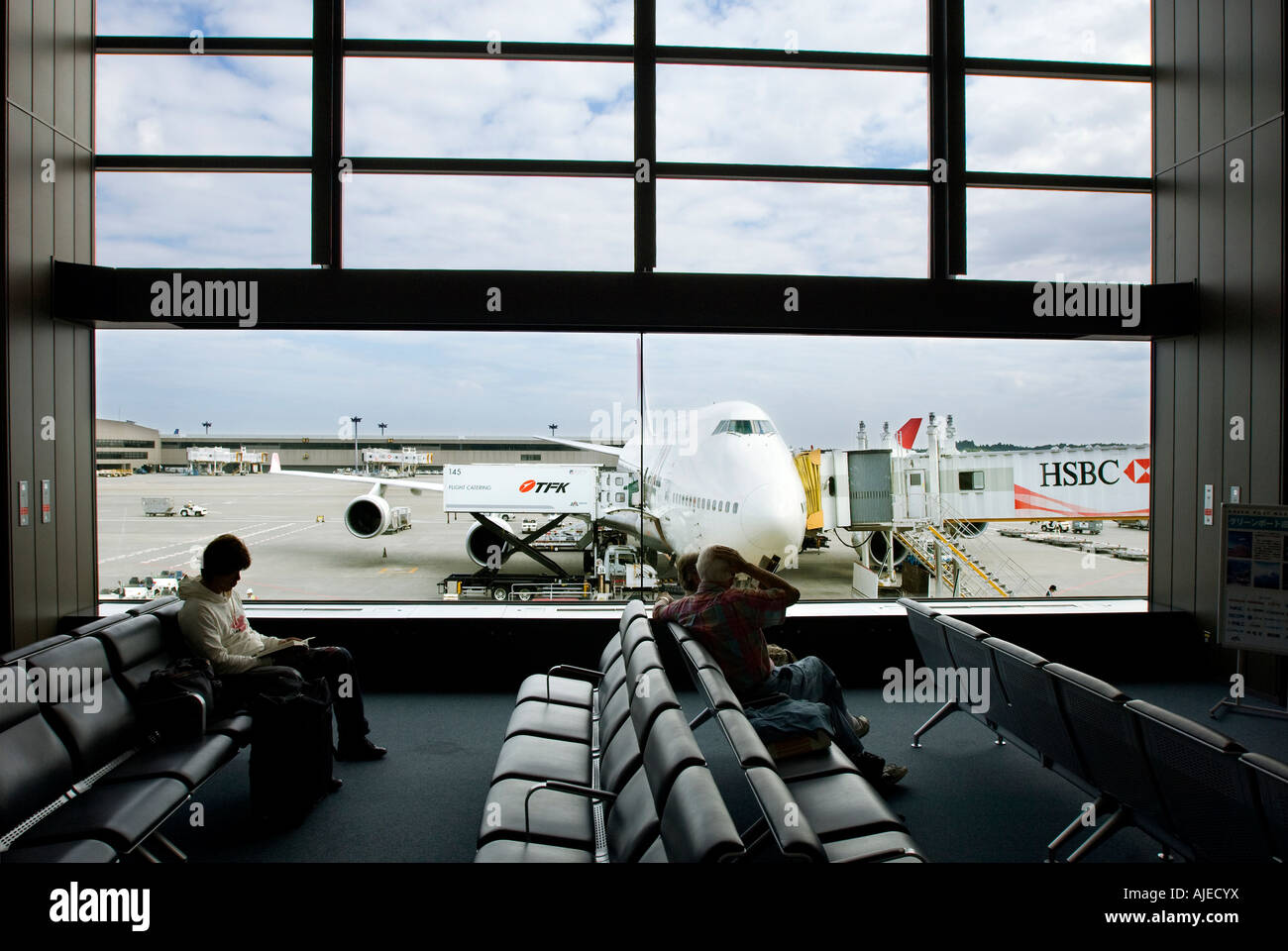 I passeggeri in attesa di Narita airport lounge di partenza , Tokyo, Giappone con un aviogetto civile in background. Foto Stock