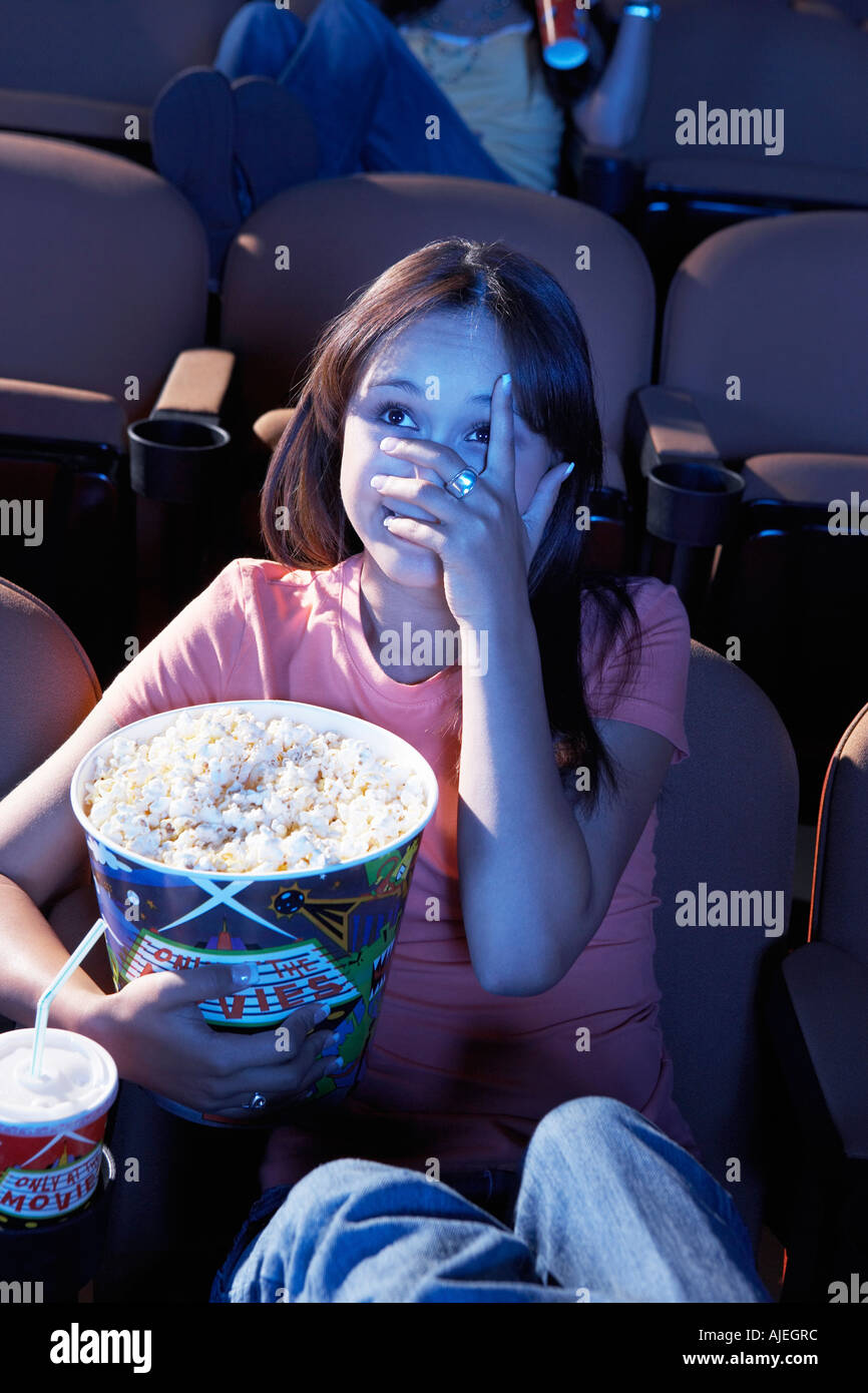 Giovane donna holding popcorn, che ricopre la faccia con la mano, guardando film in teatro Foto Stock