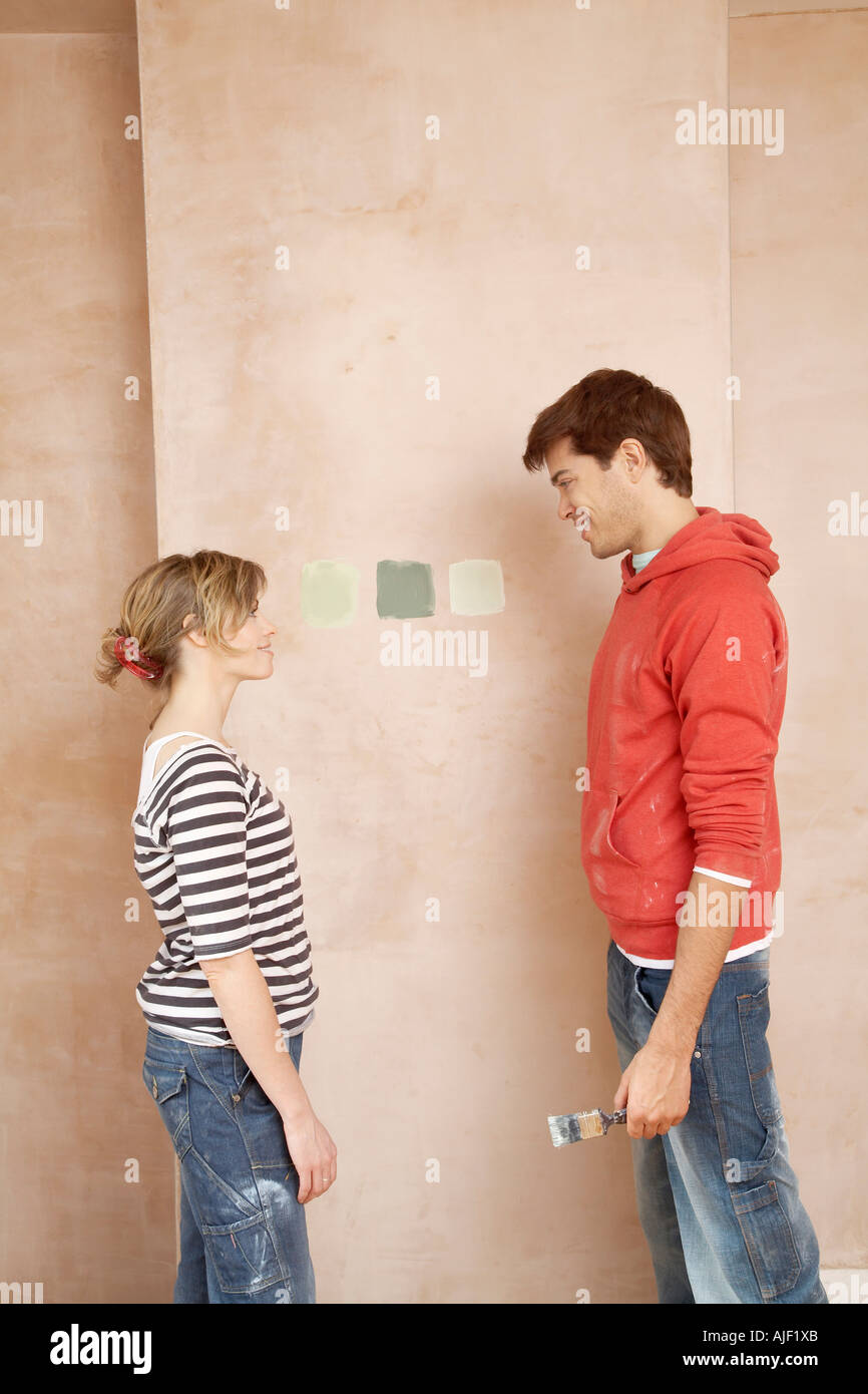 Matura in piedi faccia a faccia, scegliendo il colore della vernice campioni sulla parete Foto Stock