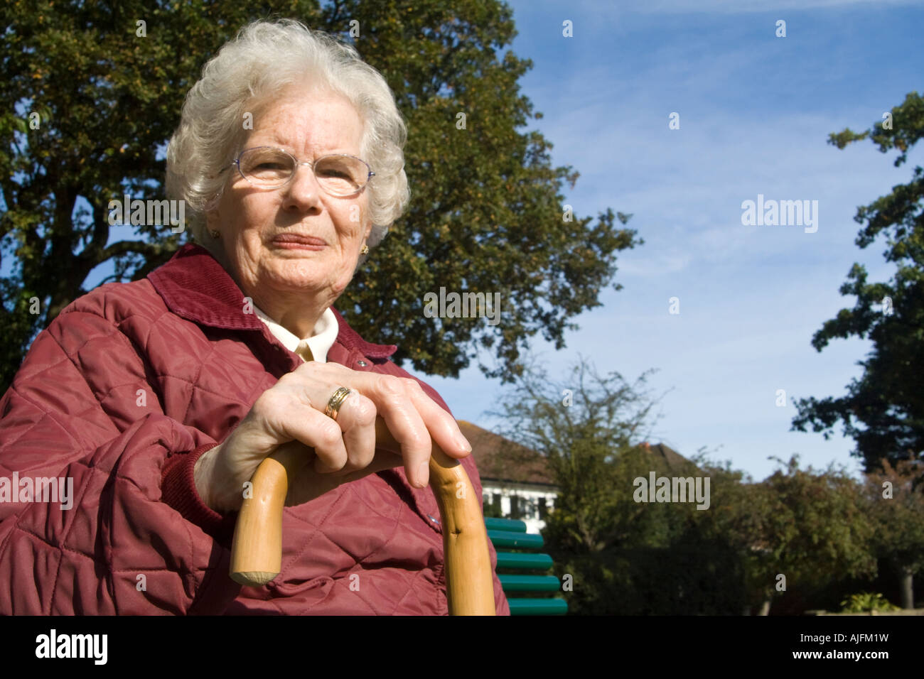 Una signora anziana con un bastone da passeggio seduta su una panchina Foto Stock