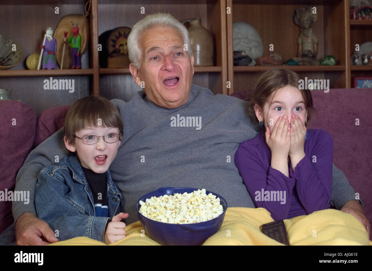 Nonno e nipoti a guardare il film spaventoso sulla televisione mangiare popcorn Foto Stock