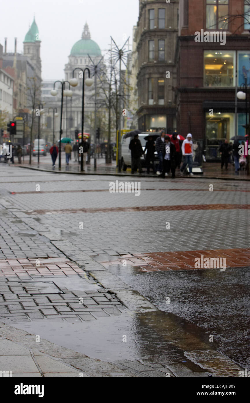 Pozza d'acqua con gocce di pioggia caduta in royal avenue a Belfast City center con la city hall e la zona dello shopping Foto Stock