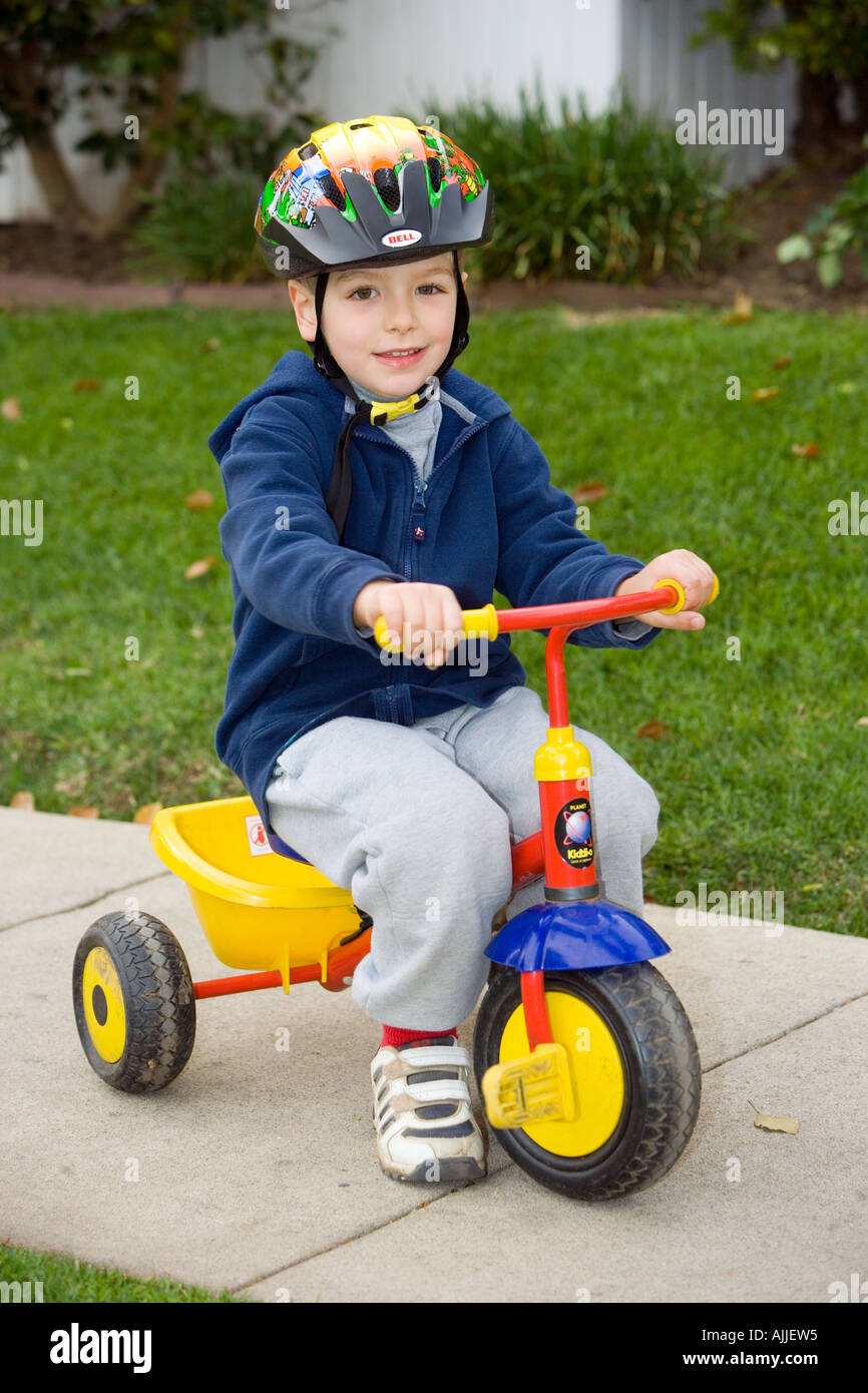 Quattro anni di vecchio ragazzo che indossa il casco cavalca il suo triciclo marciapiede verso il basso Foto Stock