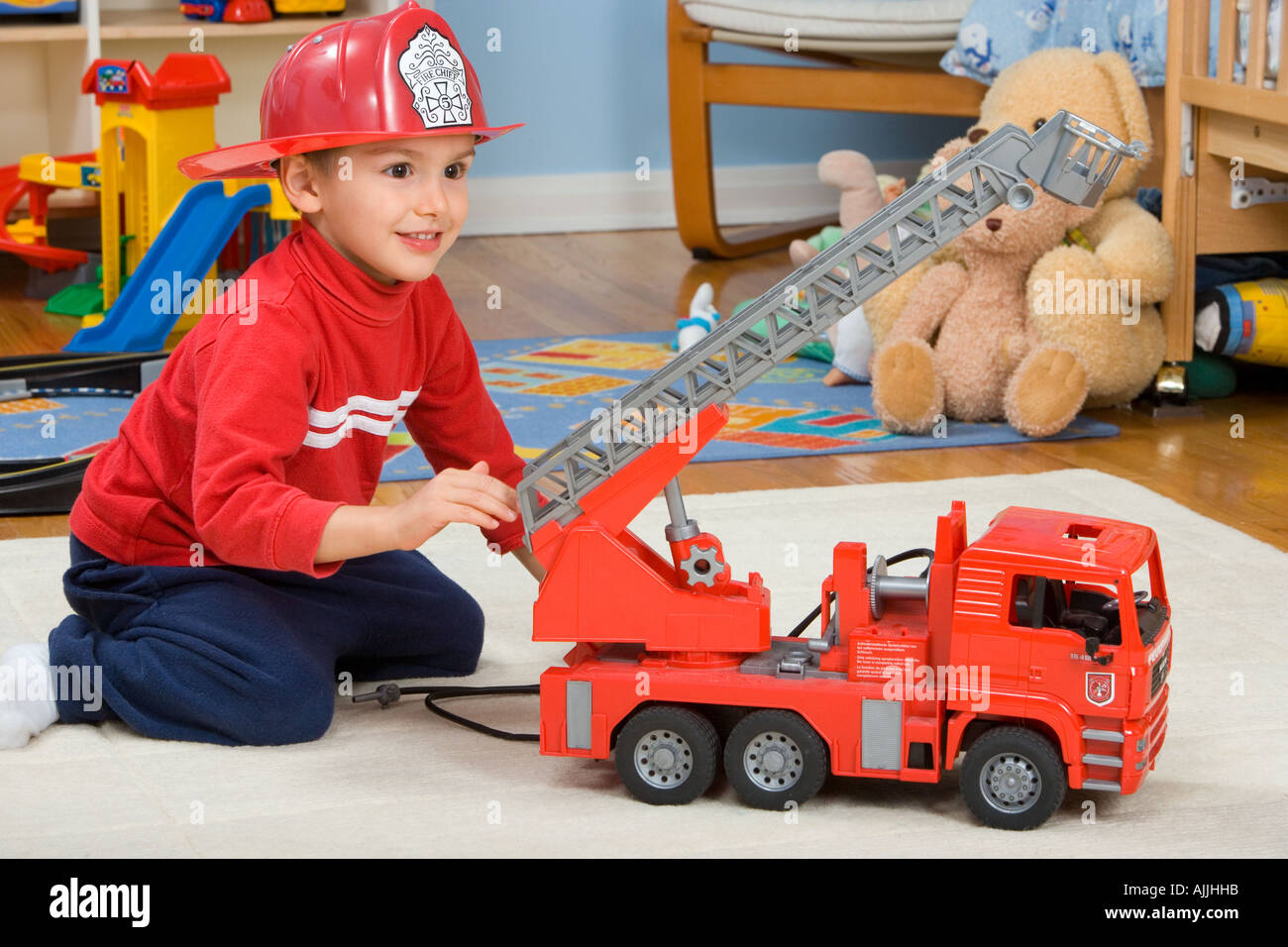 Tre anni di vecchio ragazzo indossa vigili del fuoco hat gioca con la sua big red fire carrello in camera da letto Foto Stock