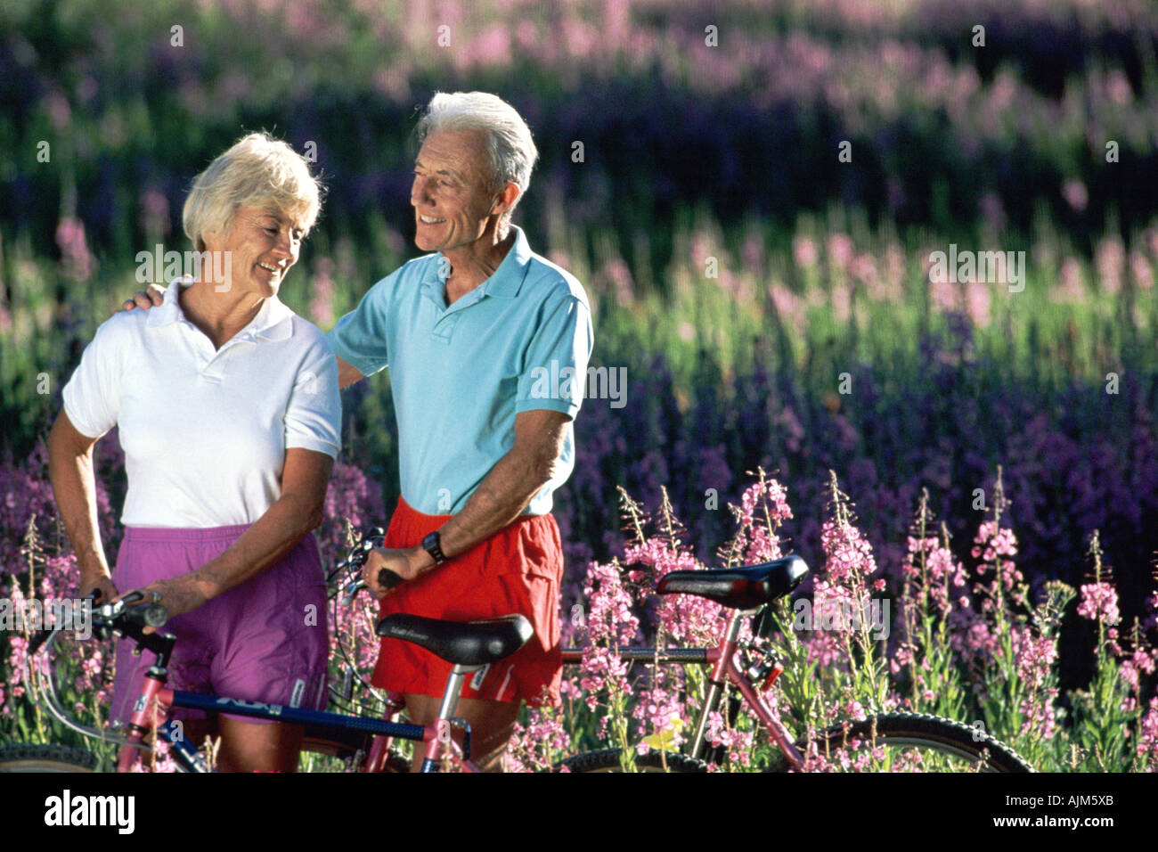 Coppia senior con la bici in campo di fiori Foto Stock Coppia senior con la bici in campo di fiori Foto Stock